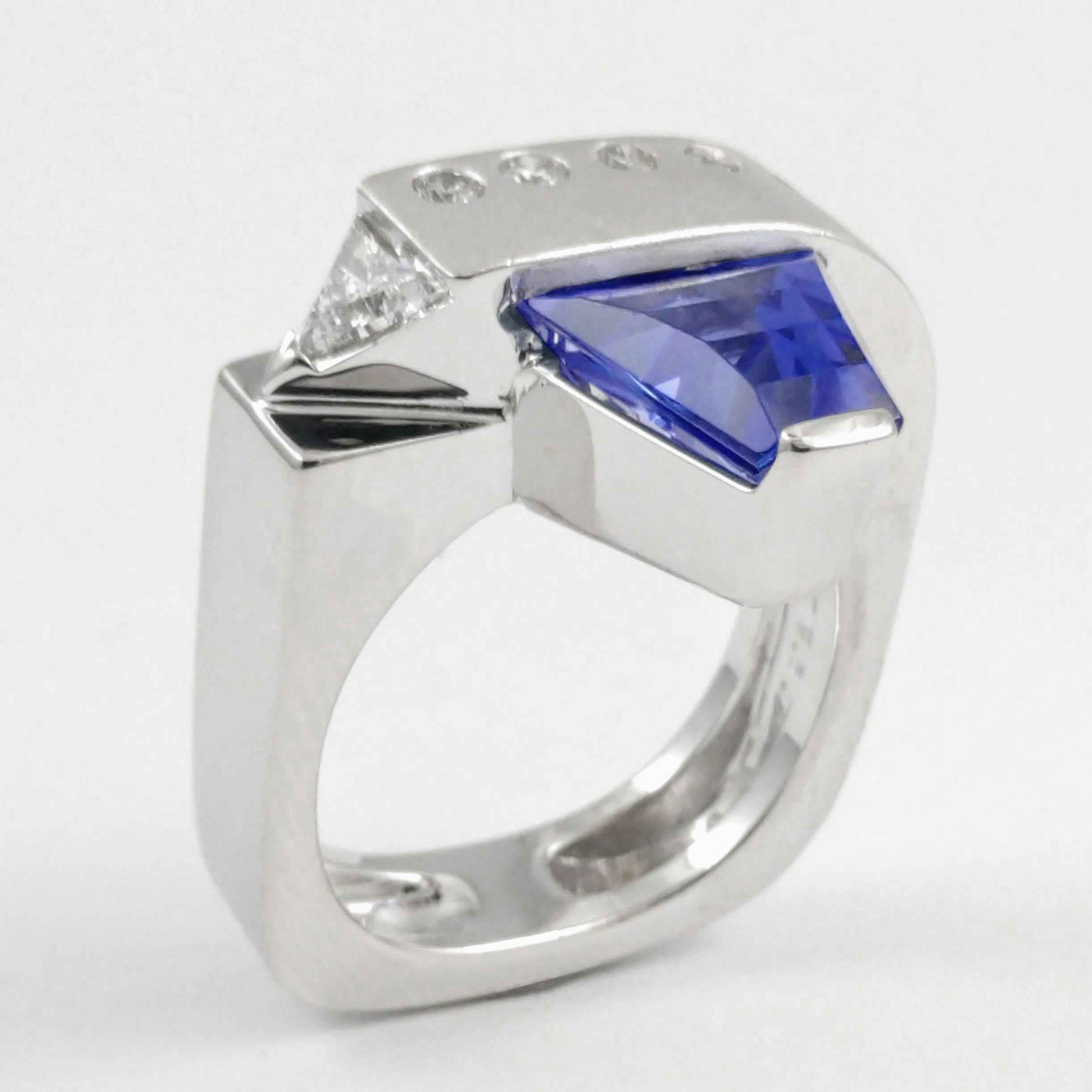 This ladies ring is distinctive and fashion-forward. Made in 18k white gold with a blue-purple fancy-cut 2.50ct Tanzanite. The ring is accented with one channel set trillion-cut diamond and six round brilliant diamonds that are each burnish set
