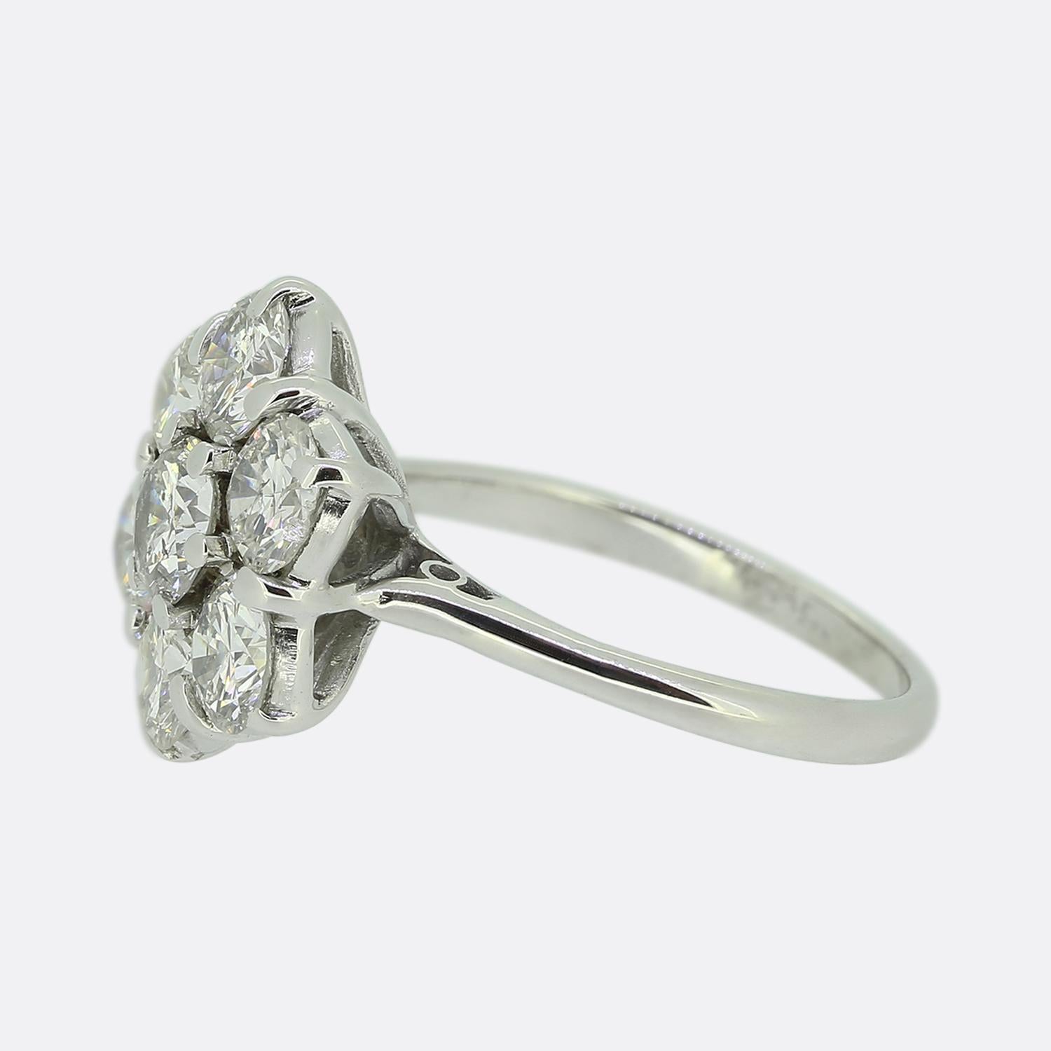 Here we have a gorgeous diamond daisy cluster ring. A single round brilliant cut diamond sits slightly risen at the centre of the face in a six-clawed setting. This principal stone is then framed around the outer edge by six perfectly matched bright