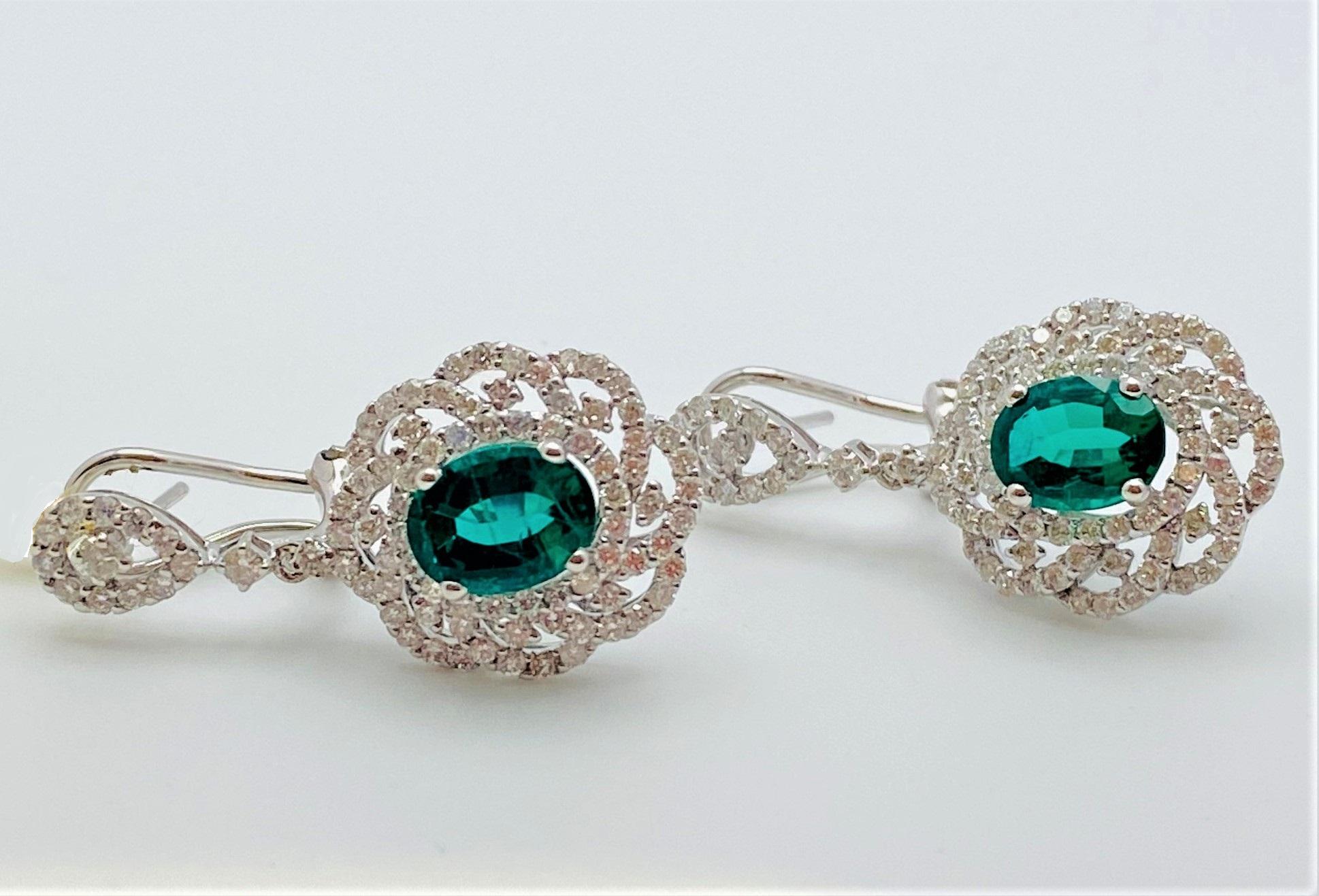 Extremely elegant emerald and diamond earrings featuring an assortment of round cut, prong set white diamonds over an oval cut emerald weighing 2.52 carats total, prong set center, enhanced buy a swirl pattern of round cut white diamonds two round