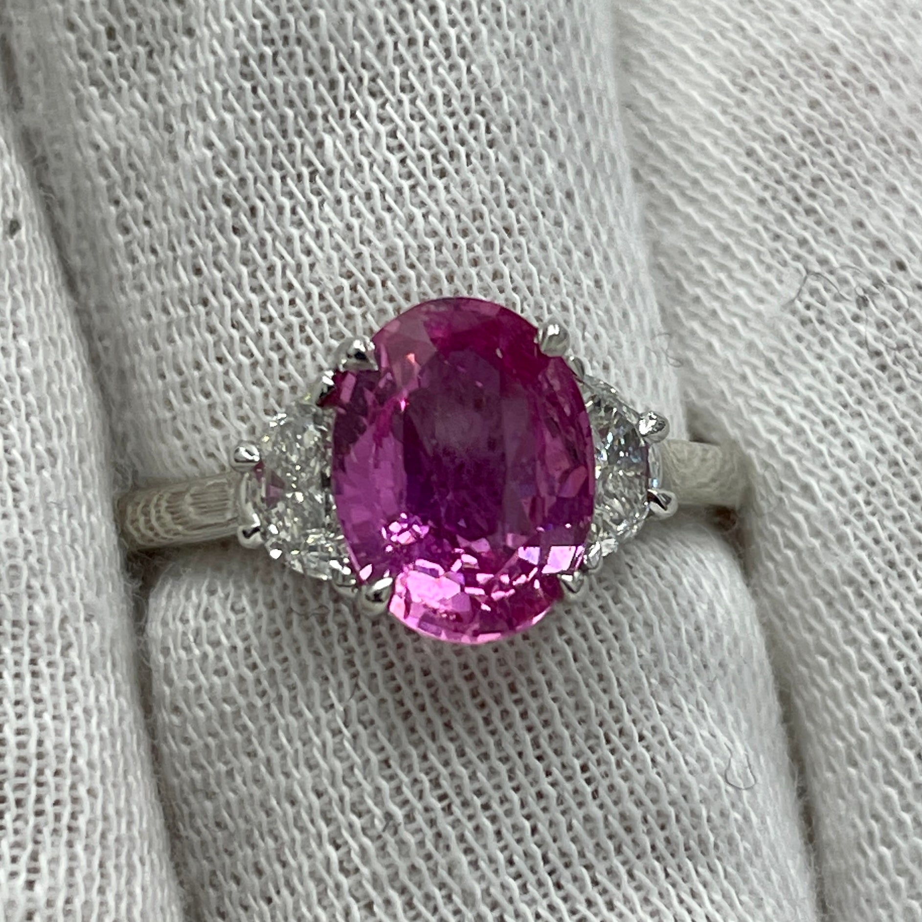 This is a bubble gum pink oval sapphire mounted in a platinum ring with 0.43Ct of brilliant white half-moon diamonds. Suitable for any occasion!