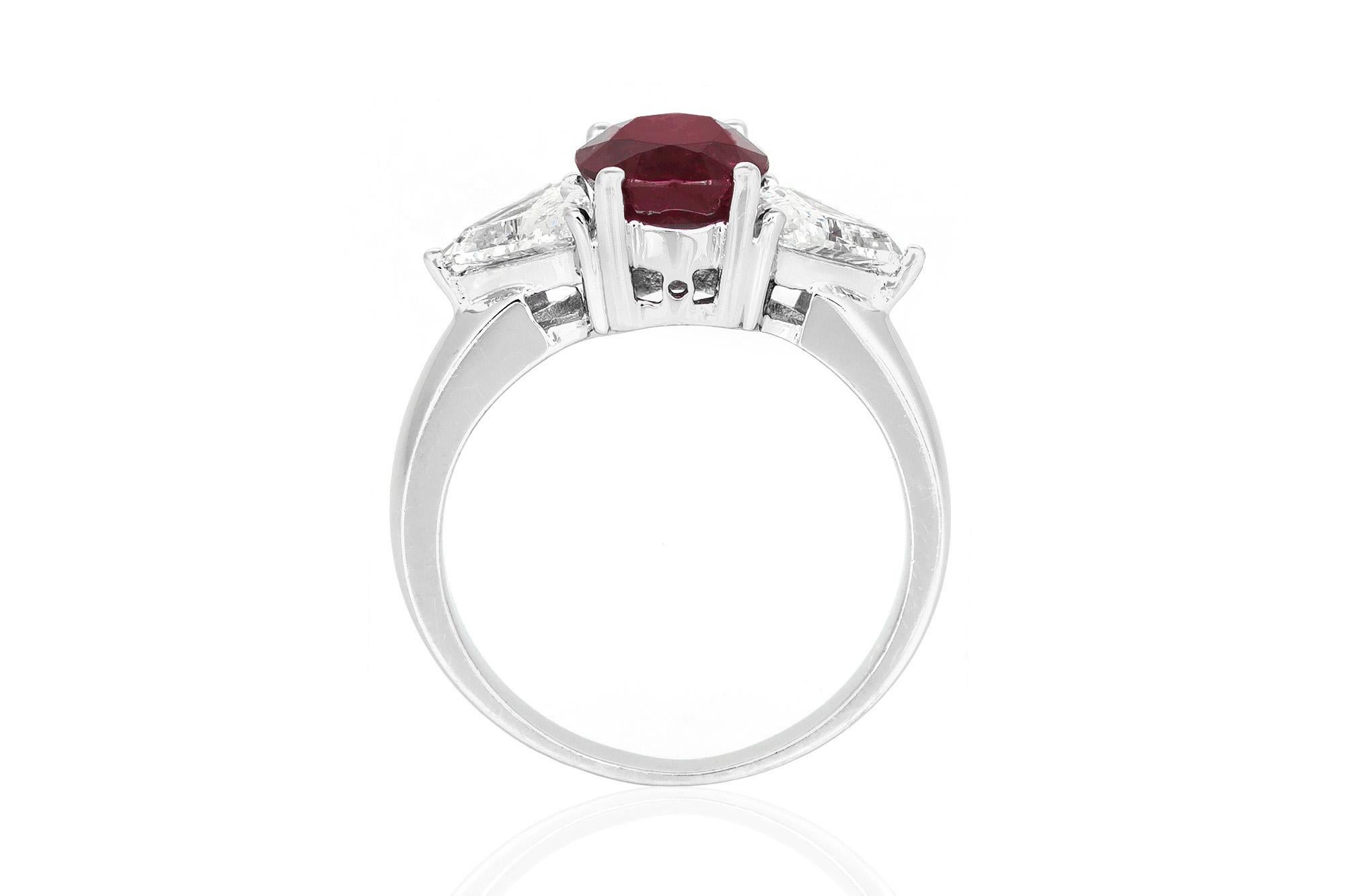 Estate ring finely crafted in 18K white gold. It features a vibrant red 2.52 carat oval shaped ruby flanked by trillion cut diamonds, weighing a total of 1.05 carat. Circa 1990's.