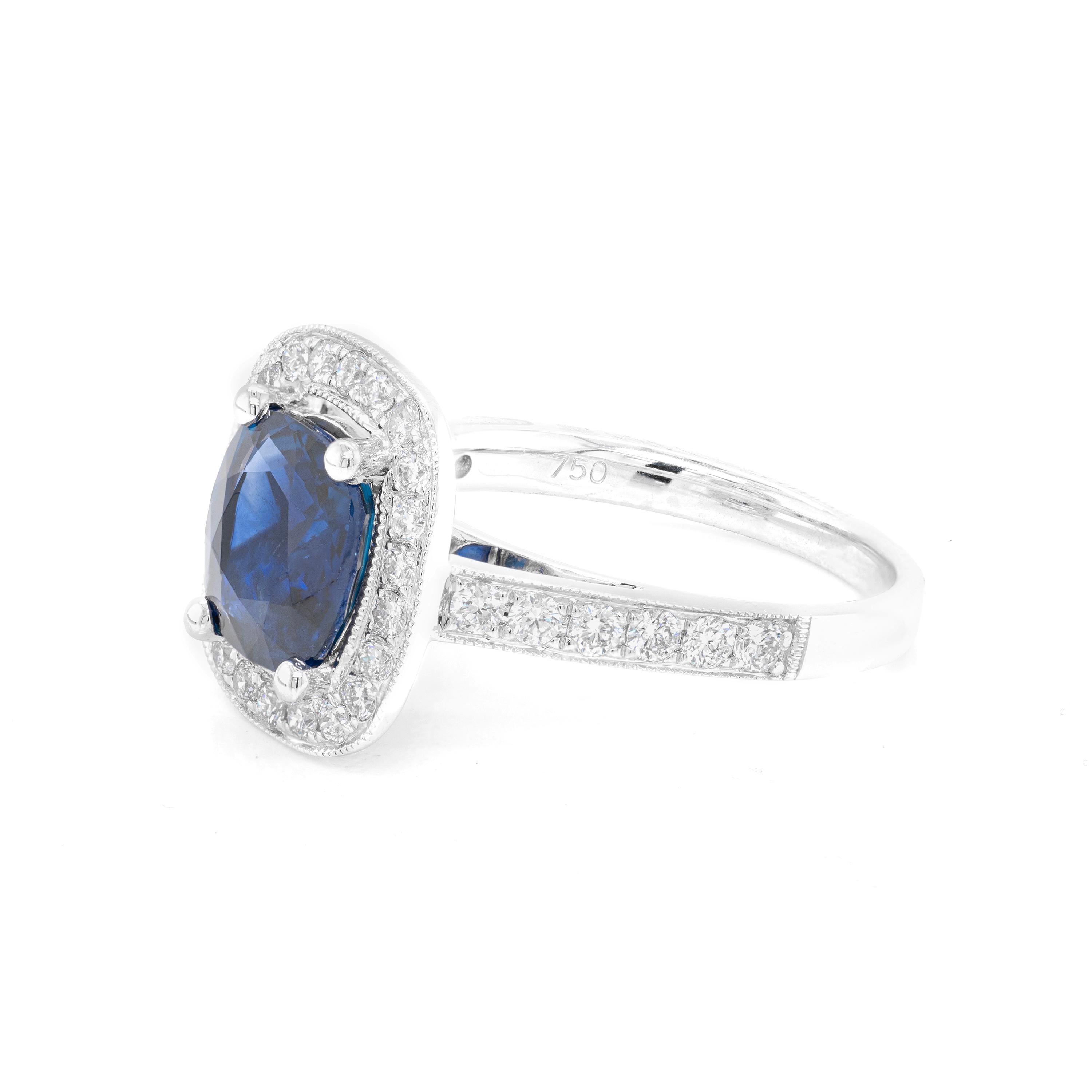 This lovely 18 carat white gold cluster ring is beautifully centred with a 2.52ct blue cushion cut sapphire, mounted in a four claw, open back setting. The vibrant stone is further highlighted by a halo of 22 round brilliant cut diamonds, all micro