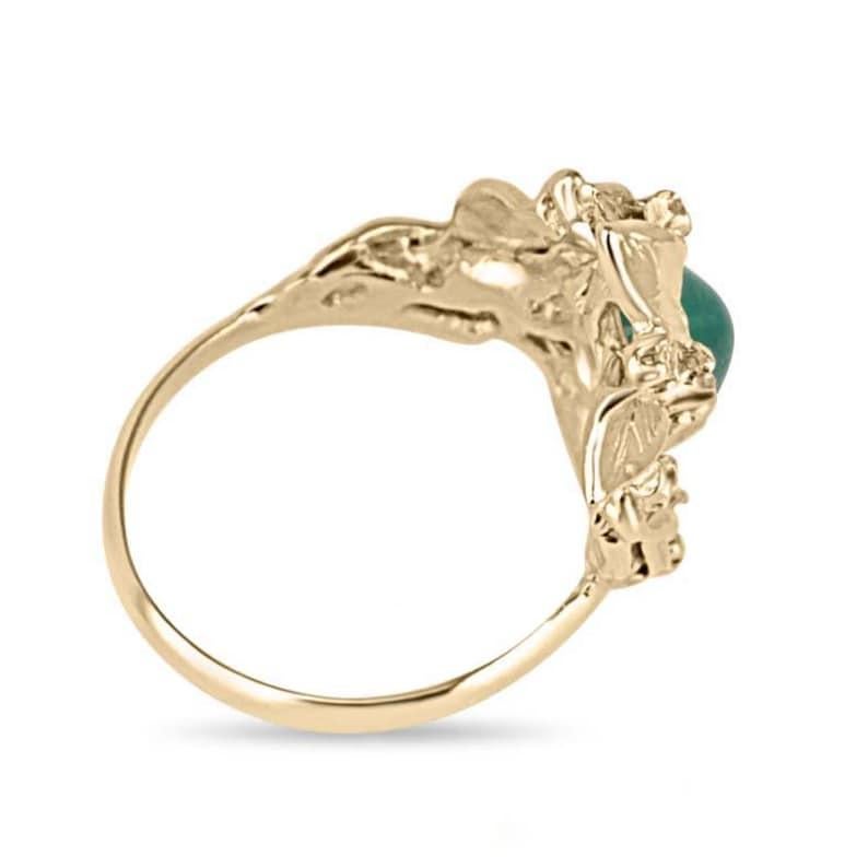 Questo incantevole anello floreale mette in mostra uno smeraldo ovale tagliato a cabochon, incastonato in quattro punte, con un'accattivante tonalità verde medio e una trasparenza traslucida. Delicate foglie d'oro, impreziosite da scintillanti