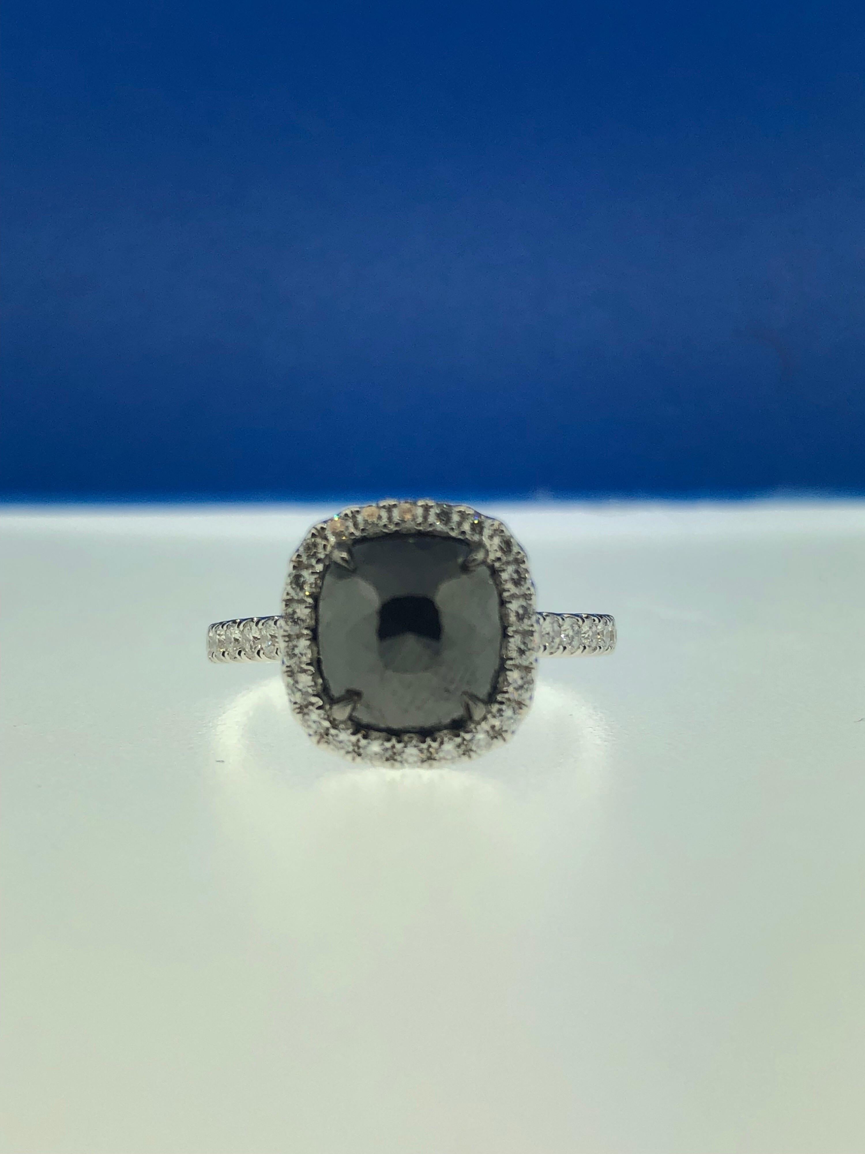 This stunning ring showcases a beautiful 2.53 carat rose cut cushion black diamond, with a white diamond halo set in 18 karat white gold. 
Total diamond weight (not including center stone) = 0.44 carats. Ring size is 6 1/2.
