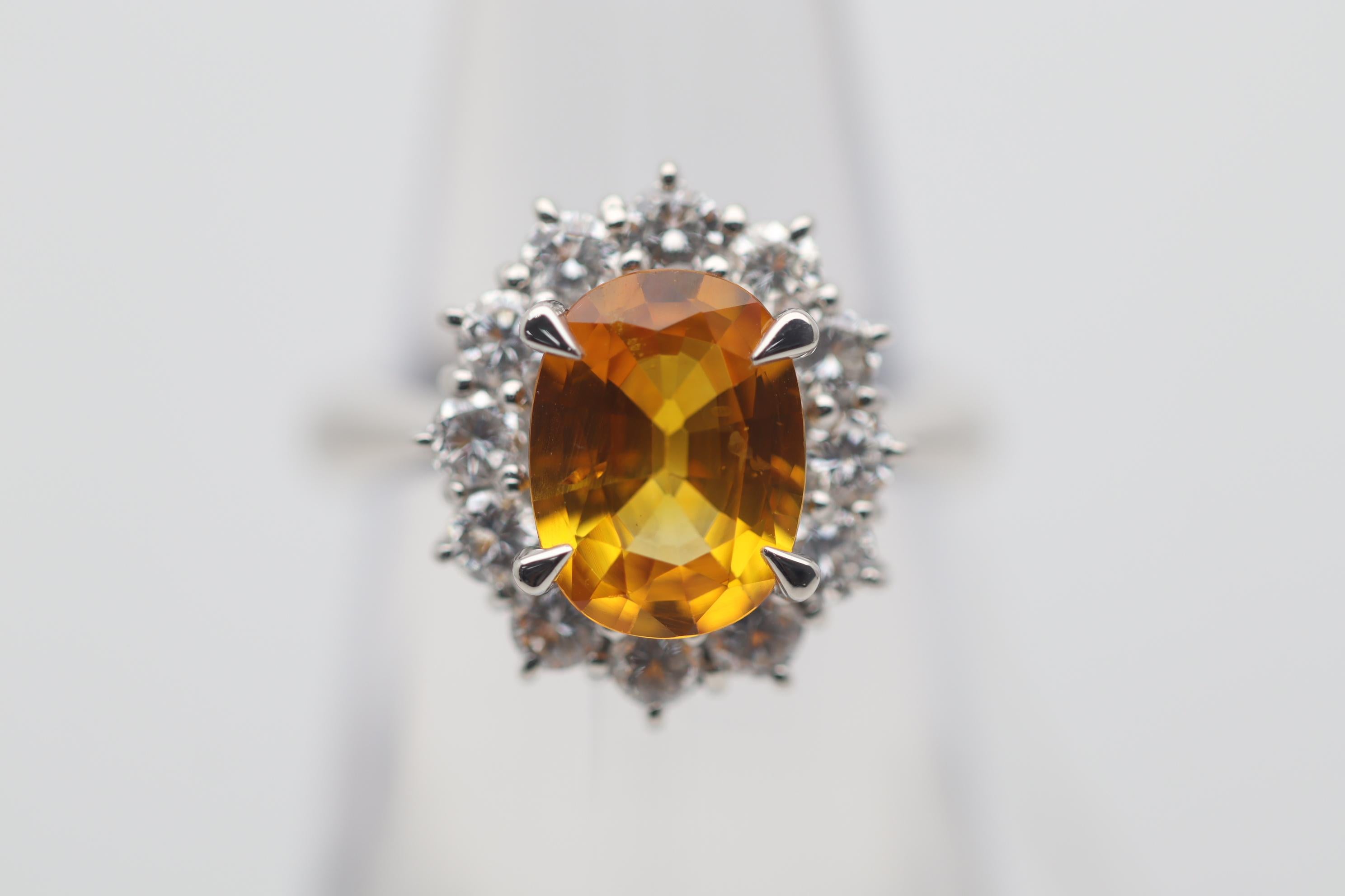 A beautiful ring featuring a bright golden orange sapphire weighing 2.54 carats. It has an intense slightly yellowish but orange color that glows in the light. It is complemented by 0.90 carats of bright white round brilliant-cut diamonds which are