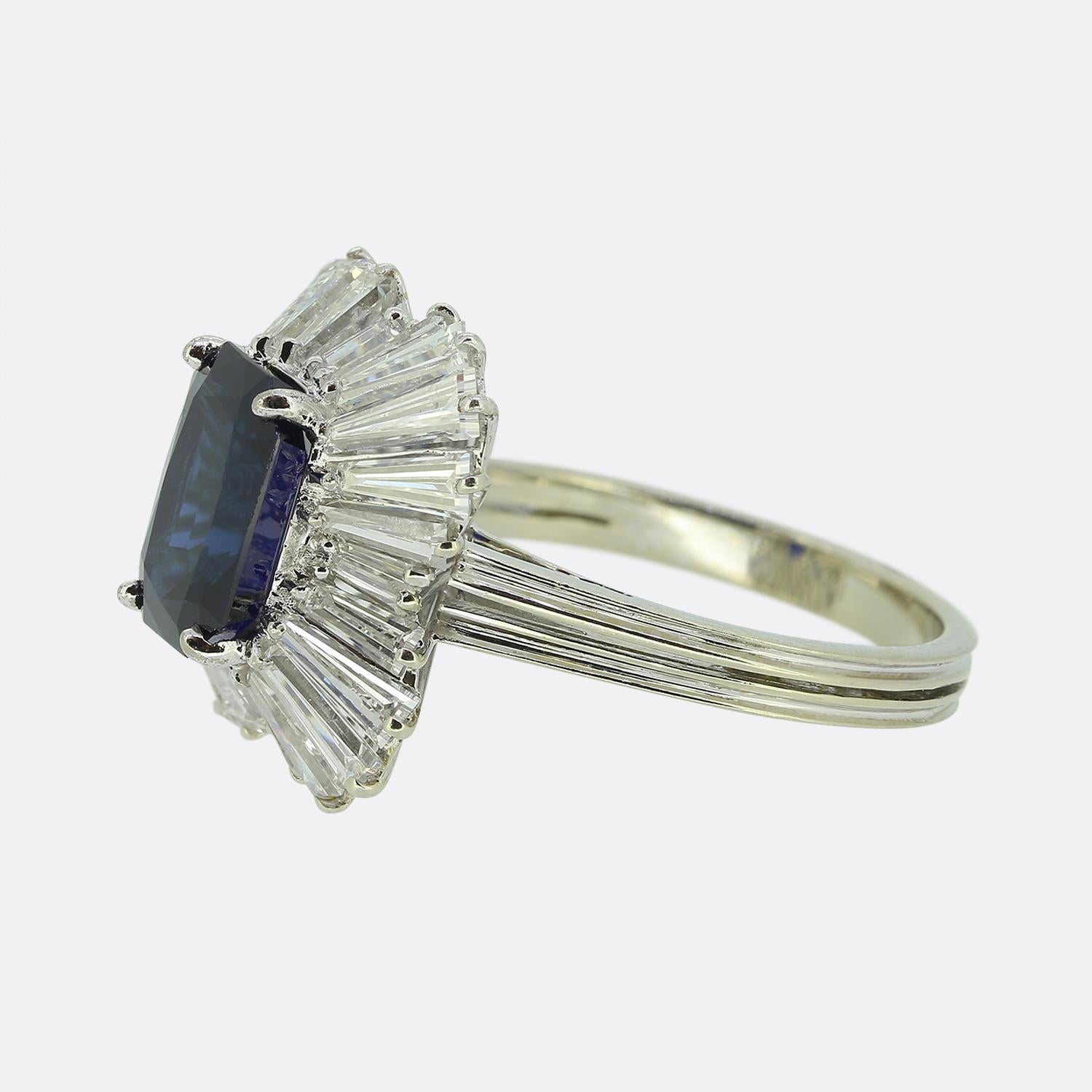 Hier haben wir einen erhabenen Ballerina-Ring mit einem tiefblauen Saphir als Herzstück. Der Saphir wird elegant von einem Kranz weißer, spitz zulaufender Diamanten im Baguetteschliff umrahmt, die ihm ein strahlendes Aussehen verleihen. Die Fassung