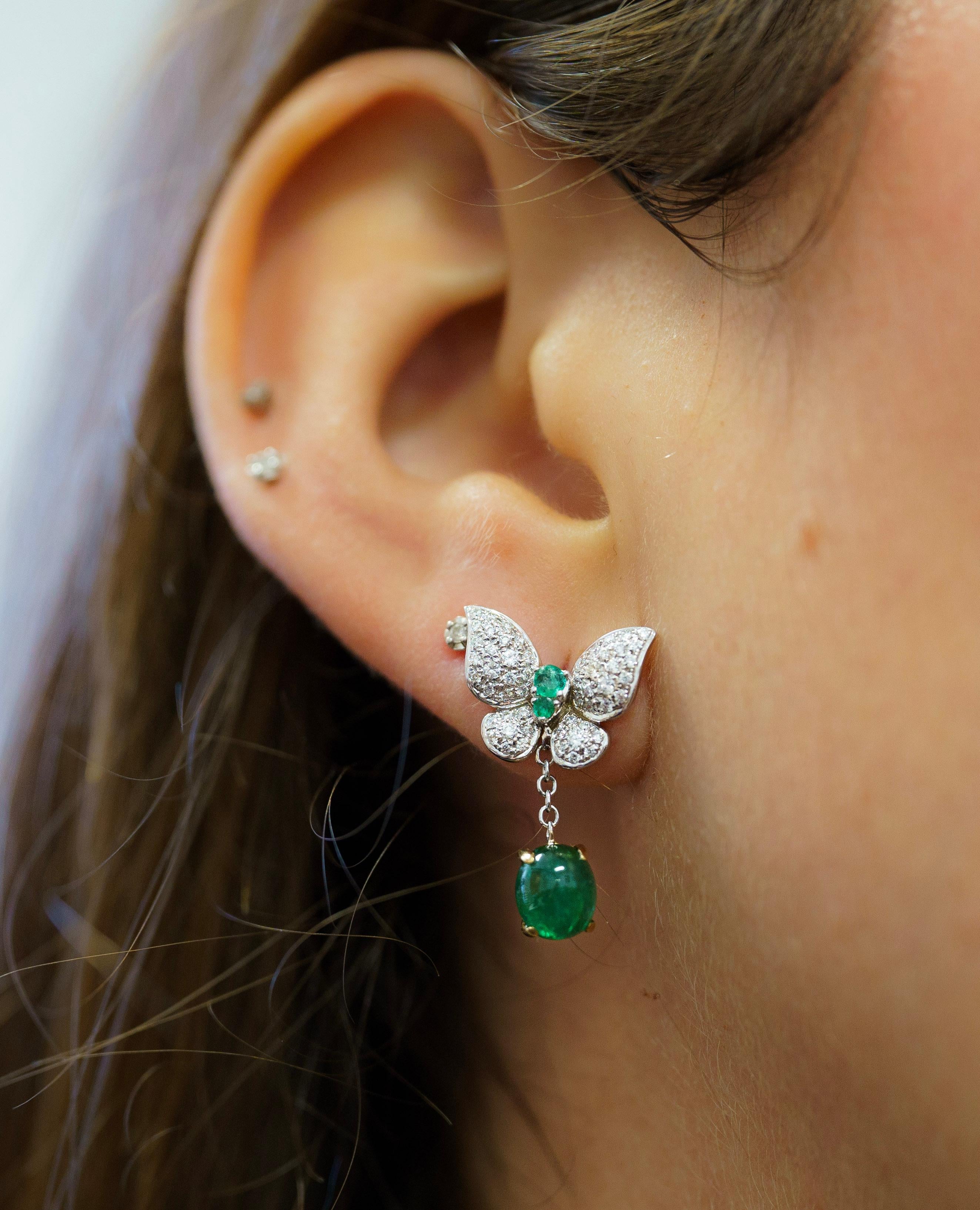 18K solid gold mounts a breathtaking pair of emerald and diamond drop earrings. Featuring two cabochon cut natural emeralds as drops and 0.50 carats in round cut white diamonds. The diamonds are pave set on a butterfly motif setting. Fixed with