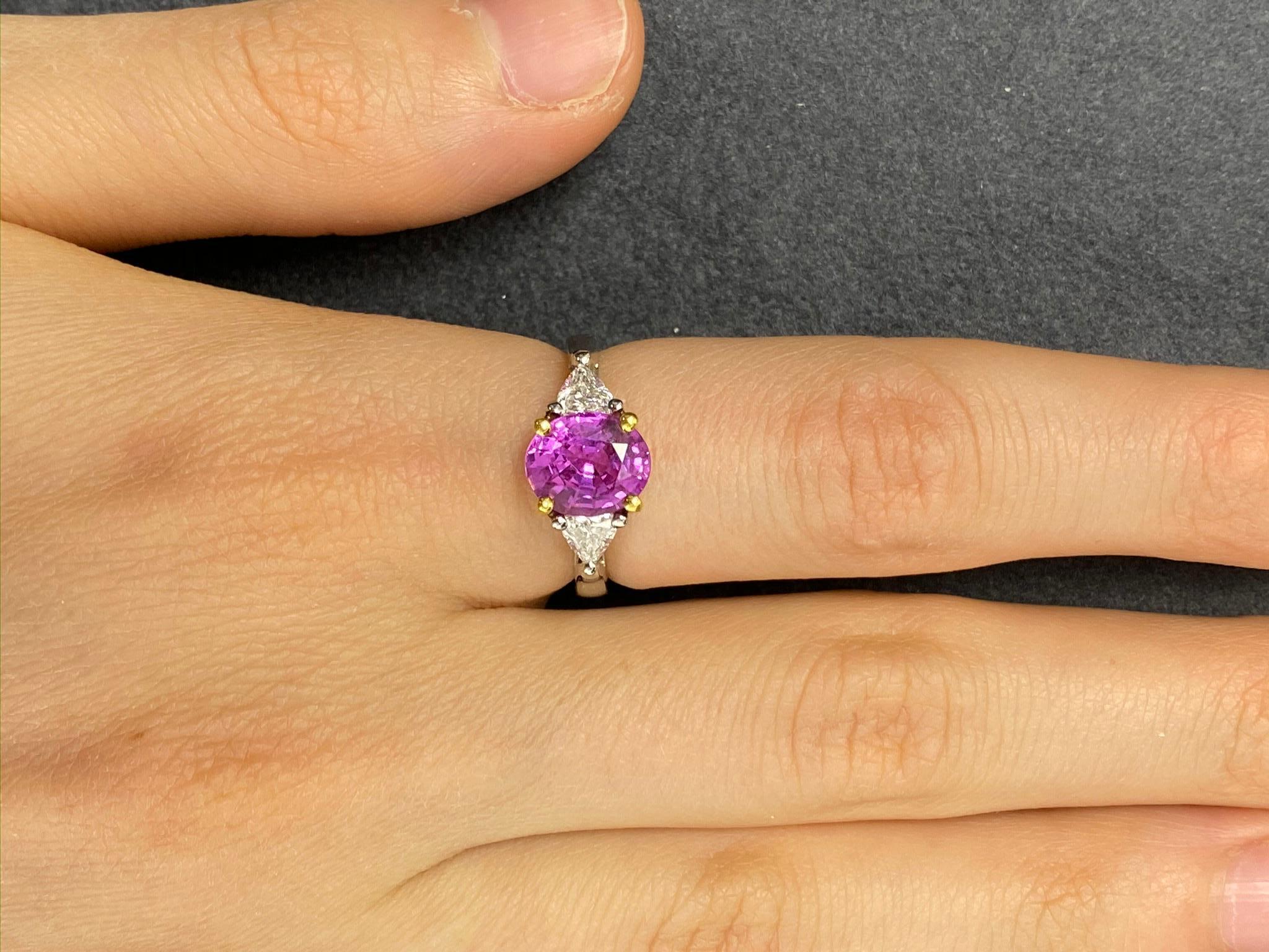 This cocktail ring showcases a stunning 2.56 carat oval hot pink sapphire set in 18 karat yellow gold basket flanked by two .25 carat trillion cut diamonds (total of .5cts) on a platinum setting and shank. Ring size is 6 1/4.