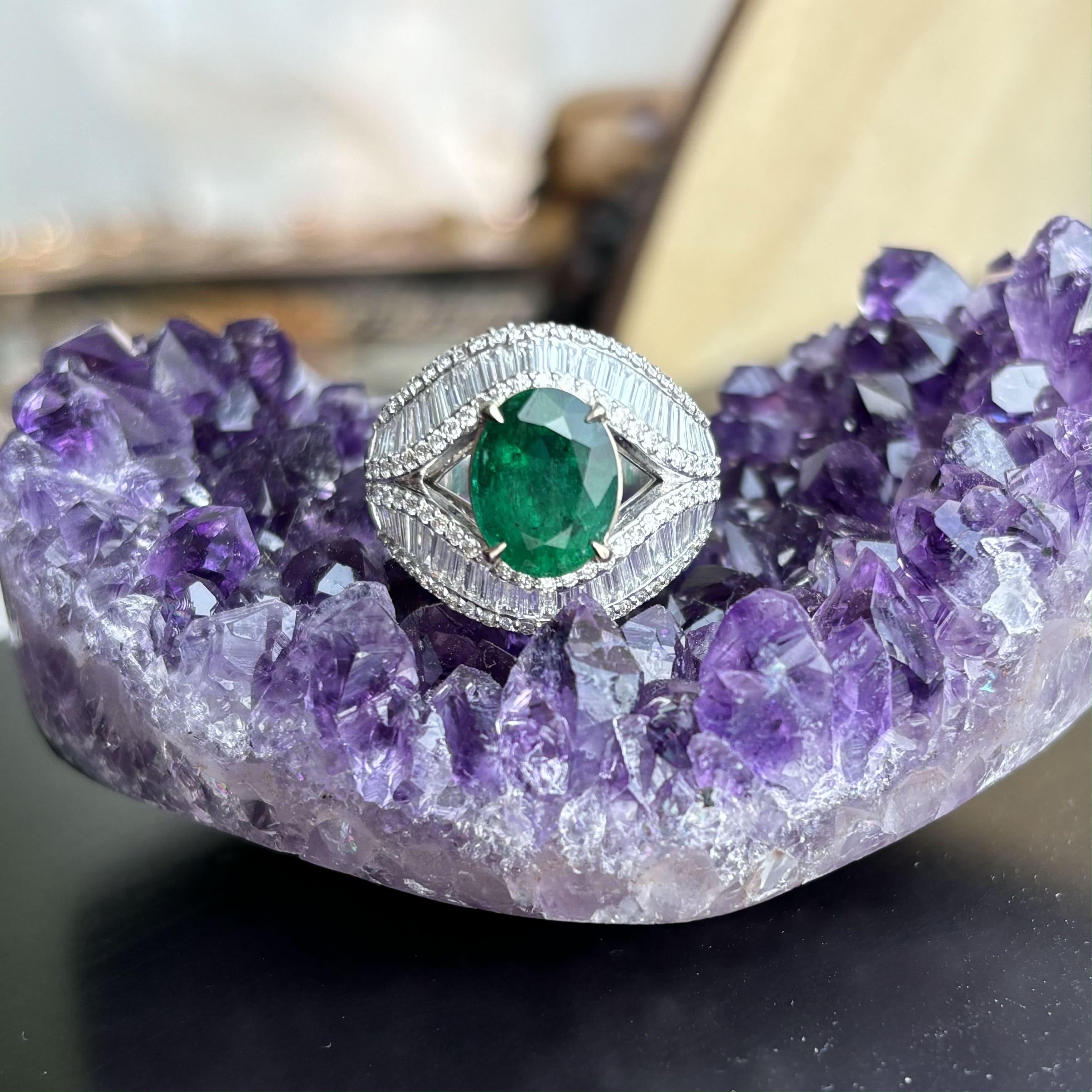 Wir präsentieren ein Meisterwerk von einem Ring, der die lebhafte grüne Eleganz eines sorgfältig geschliffenen Smaragds mit der Brillanz funkelnder Baguette-Diamanten perfekt kombiniert.

Der 2.56-karätige Smaragd stammt aus den bezaubernden Minen