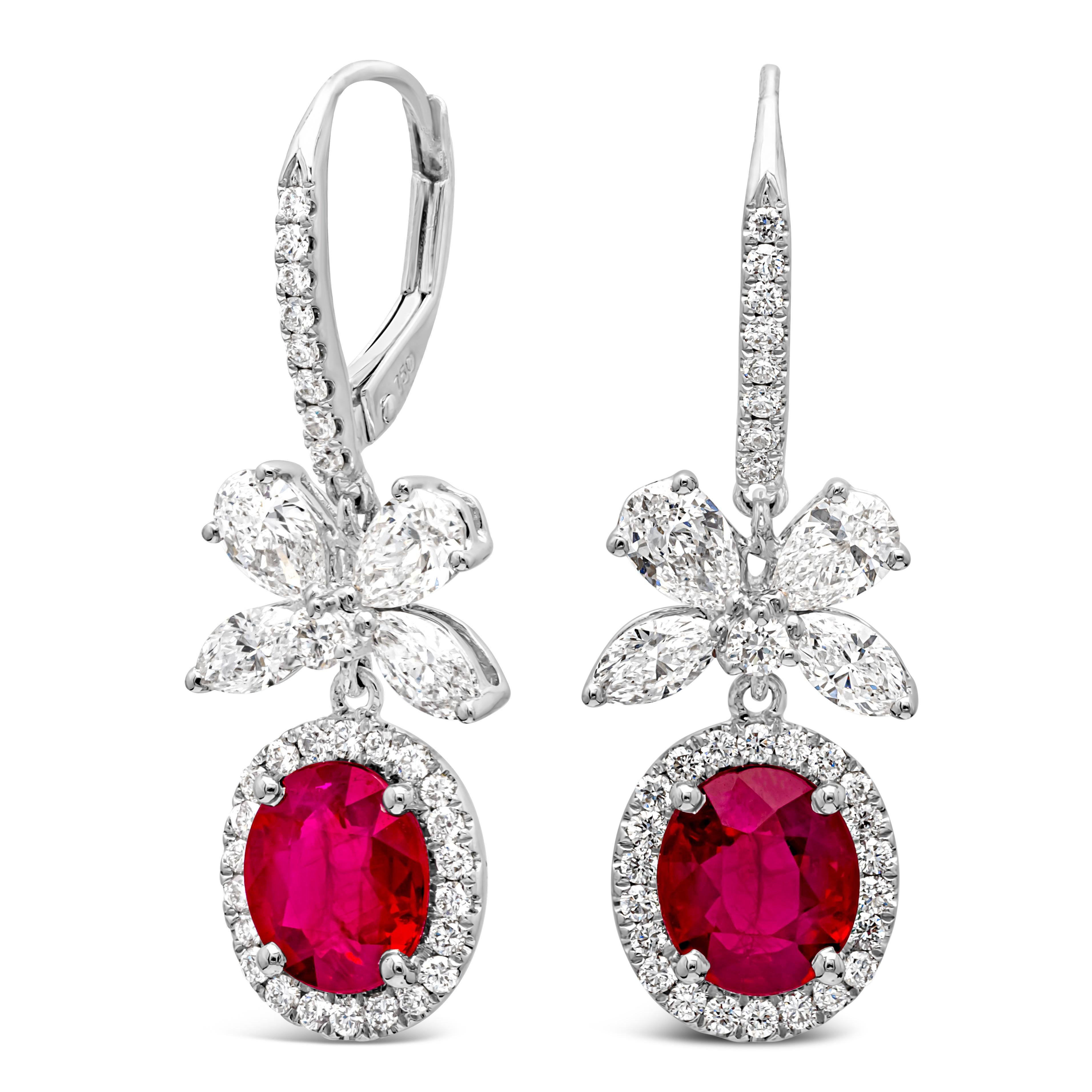 These gorgeous pair of dangle earrings feature an oval cut color-rich ruby in the center weighing 2.56 carats total, surrounded by a row of brilliant round diamonds in a halo design. A bow-like figure made with diamonds hang on top of the ruby halo