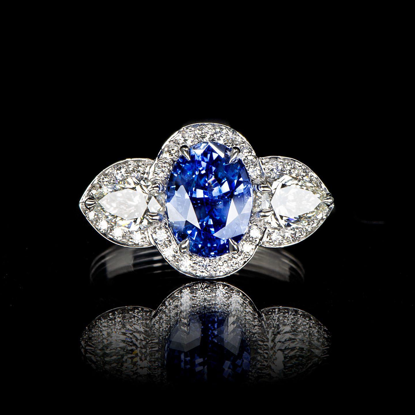 This cluster engagement ring showcases a stunning oval Ceylon Blue Sapphire weighing 2.57 carats in the centre flanked by pear-shaped diamonds (total weight of 0.78 carat, Colour F/G, Clarity VS) with all three surrounded by round brilliant diamonds