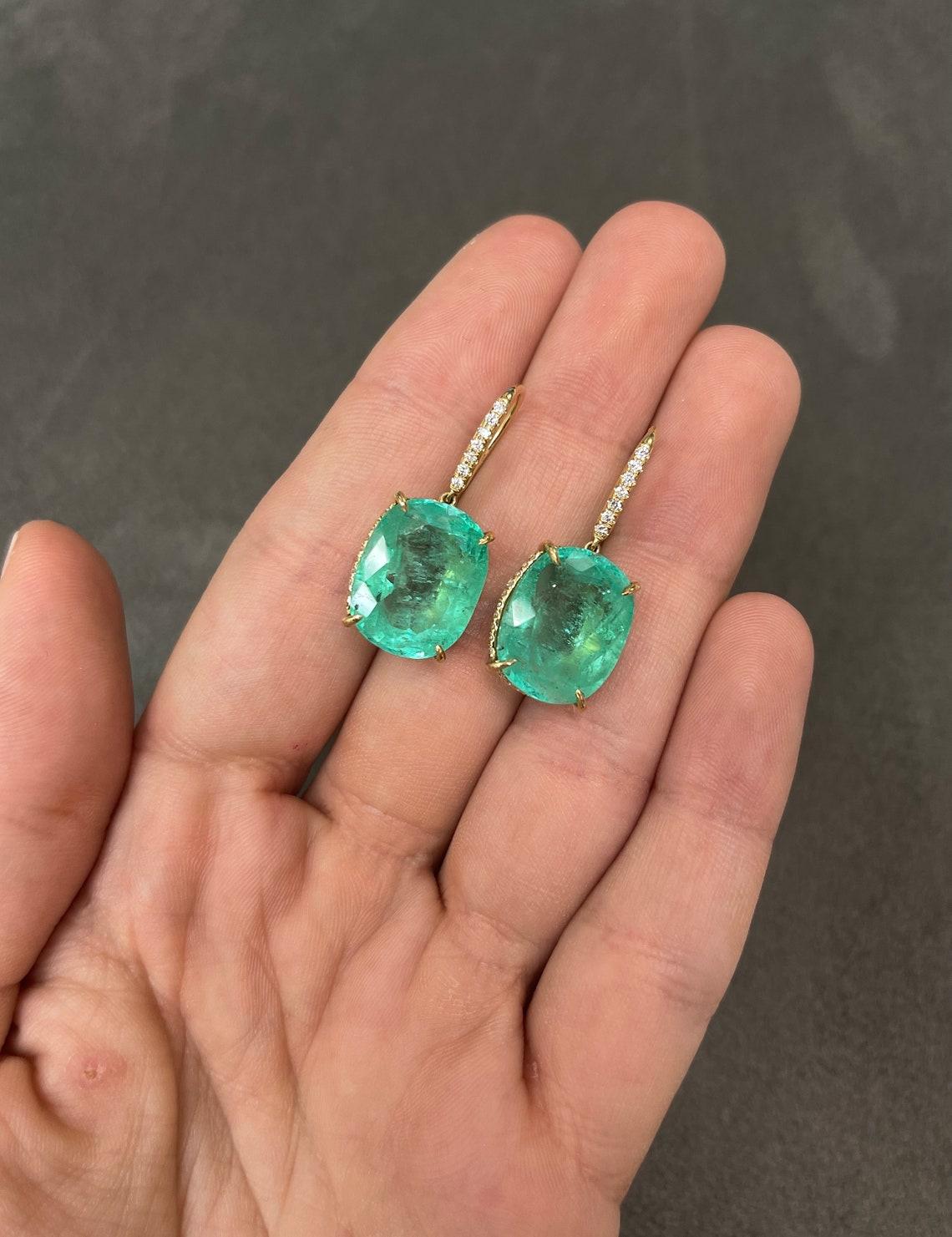 Large cushion cut Colombian emerald and diamond accent dangling earrings in fine 18K yellow gold. Displayed are medium-green cushion emeralds with very good transparency, accented by a simple prong gold mount, allowing for the emeralds to be shown