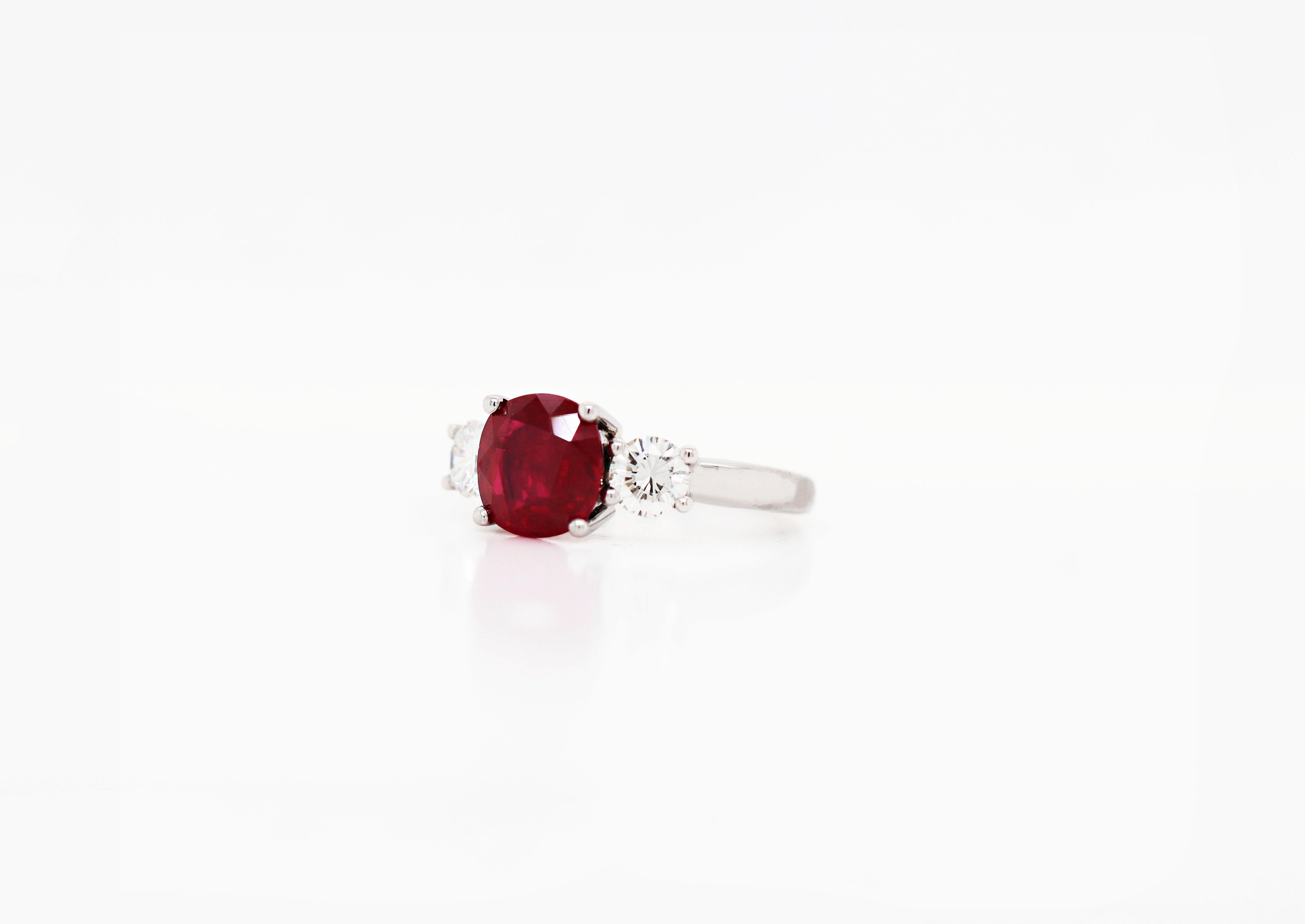 This beautiful three stone ring features a rich red cushion cut ruby weighing 2.58ct in a four claw open back setting. The vibrant stone is accompanied by two fine quality round brilliant cut diamonds weighing a combined weight of 0.72ct in four