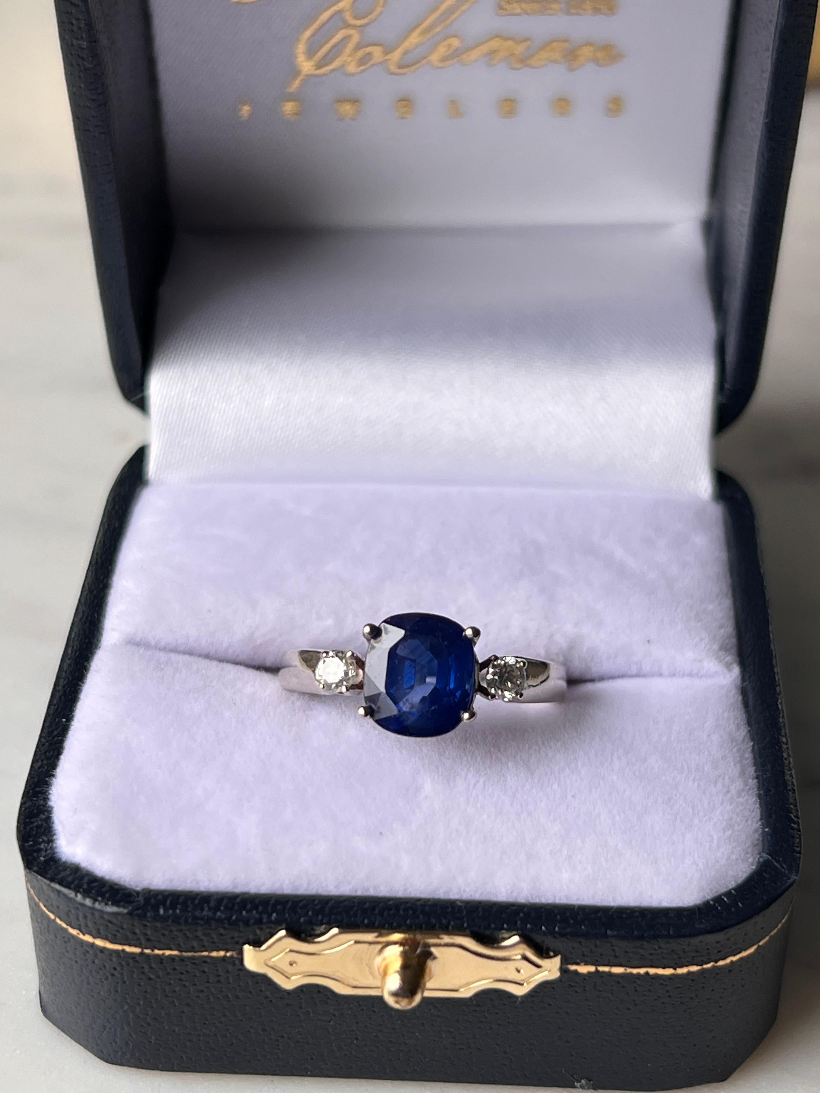 Questo elegante anello in oro bianco 18 carati presenta uno zaffiro blu taglio cuscino riccamente saturo del peso di circa 2,59 carati. Lo zaffiro è affiancato da due diamanti tondi taglio brillante per un totale di circa 0,19 carati, con colore H-I