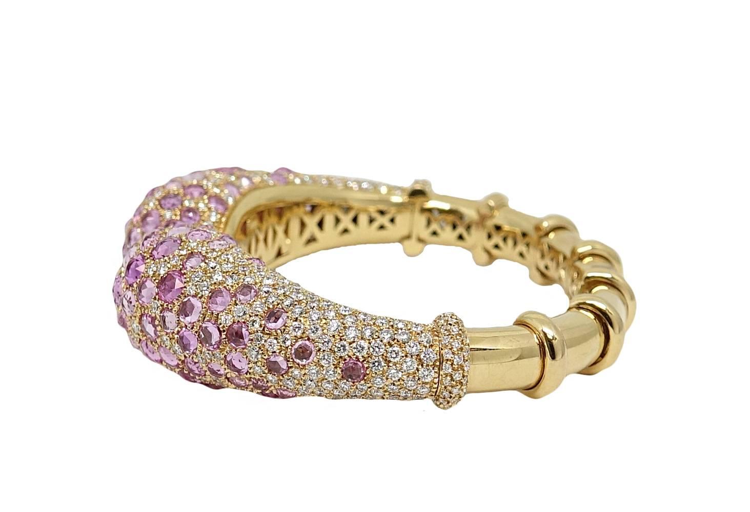 This Absolutely Stunning 18K Yellow Gold Bangle Has Sporadic Vibrant Pink Sapphires Covering The Tear Drop Shaped Opening Of This Bangle and Weigh A Total Carat Weight Of 25.98 Carats. Small Sparkling Round Diamonds Are Irregularly Placed Around The