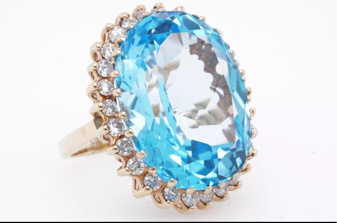 Make a bold statement with this breathtaking Swiss Blue Topaz cocktail ring, featuring a stunning 25-carat oval-cut gemstone that radiates brilliant sky-blue color and exceptional clarity. The topaz is expertly set in gleaming 14K yellow gold,