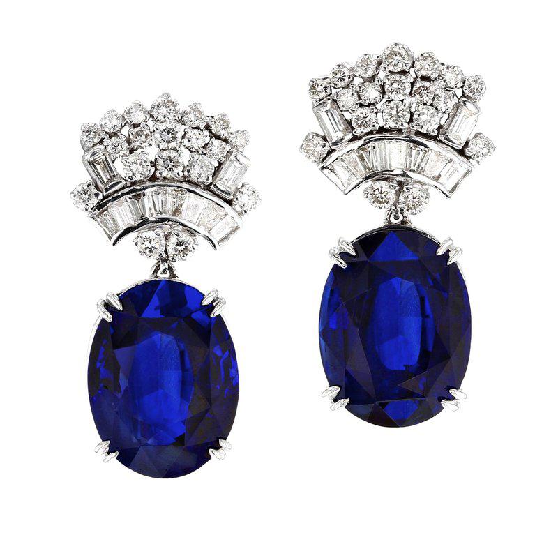 A large and classic pair of dangle earrings set with large mixed-cut oval shape sapphires weighing over thirteen carats each suspended from a floral design clip set with thirty-eight round brilliant-cut and twenty baguette diamonds, set in 18k white