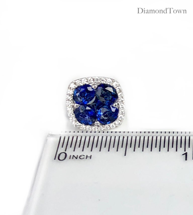 These stud earrings feature a cluster center of blue sapphires (five stones per earring, total weight 2.6 carats) surrounded by a halo of round white diamonds (total diamond weight 0.21 carats), set in 18k white gold.

A matching pendant is also