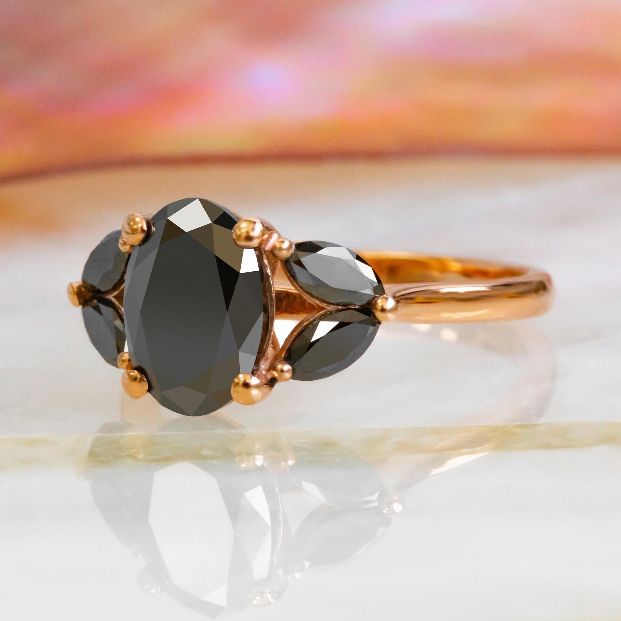Unique black Diamond engagement ring set with Oval cut black diamond center stone in 14K Rose gold ring sided by opaque black Marquise diamonds creating a beautiful multi-shaped ring from DianaRafael's DianaBlackIce Natural Black Diamond Jewelry