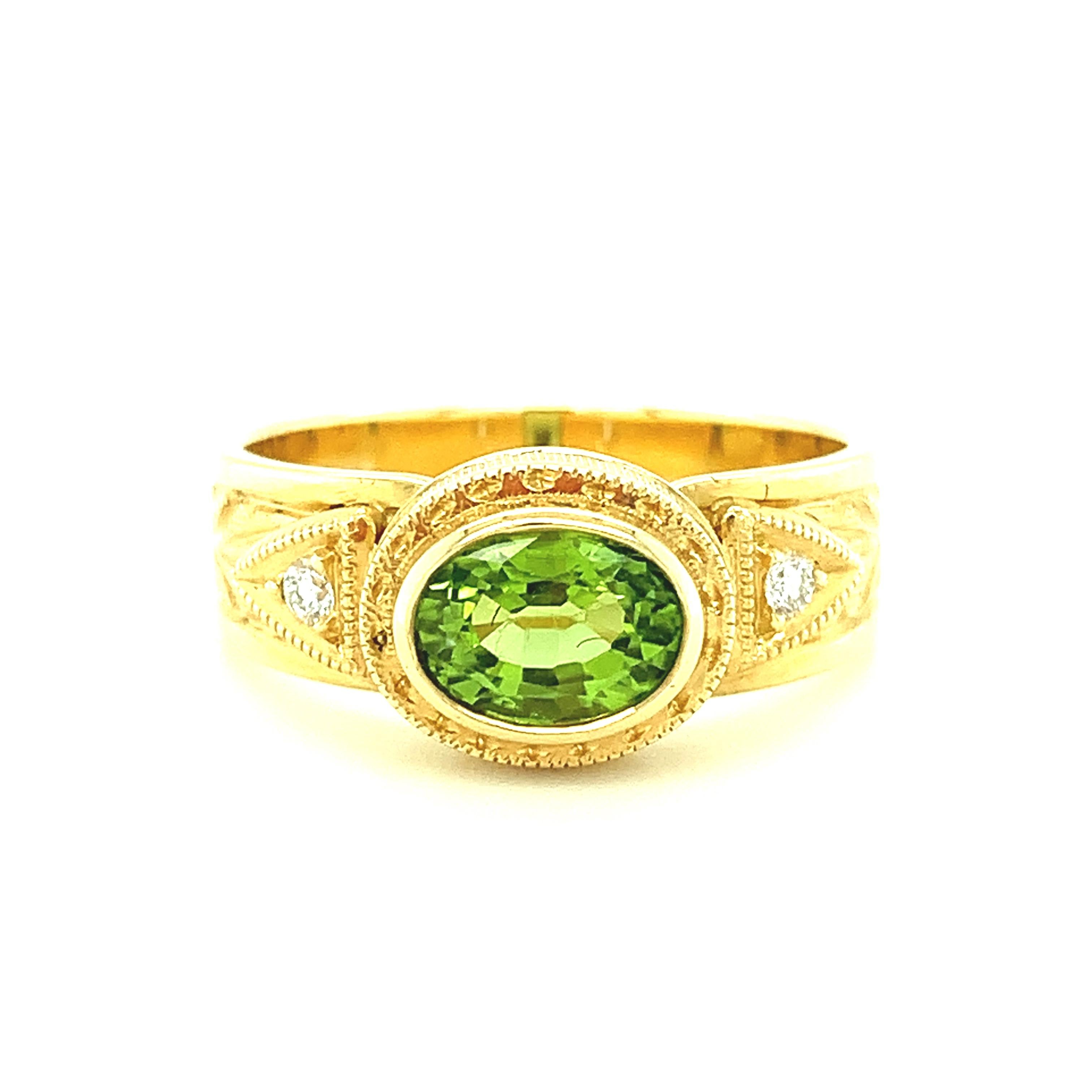 This pretty ring features a very bright, sparkling peridot that has been set in an intricately handmade 18k yellow gold bezel. The oval peridot has exceptional brilliance and is accented by two sparkling, round brilliant white diamonds. The sides of