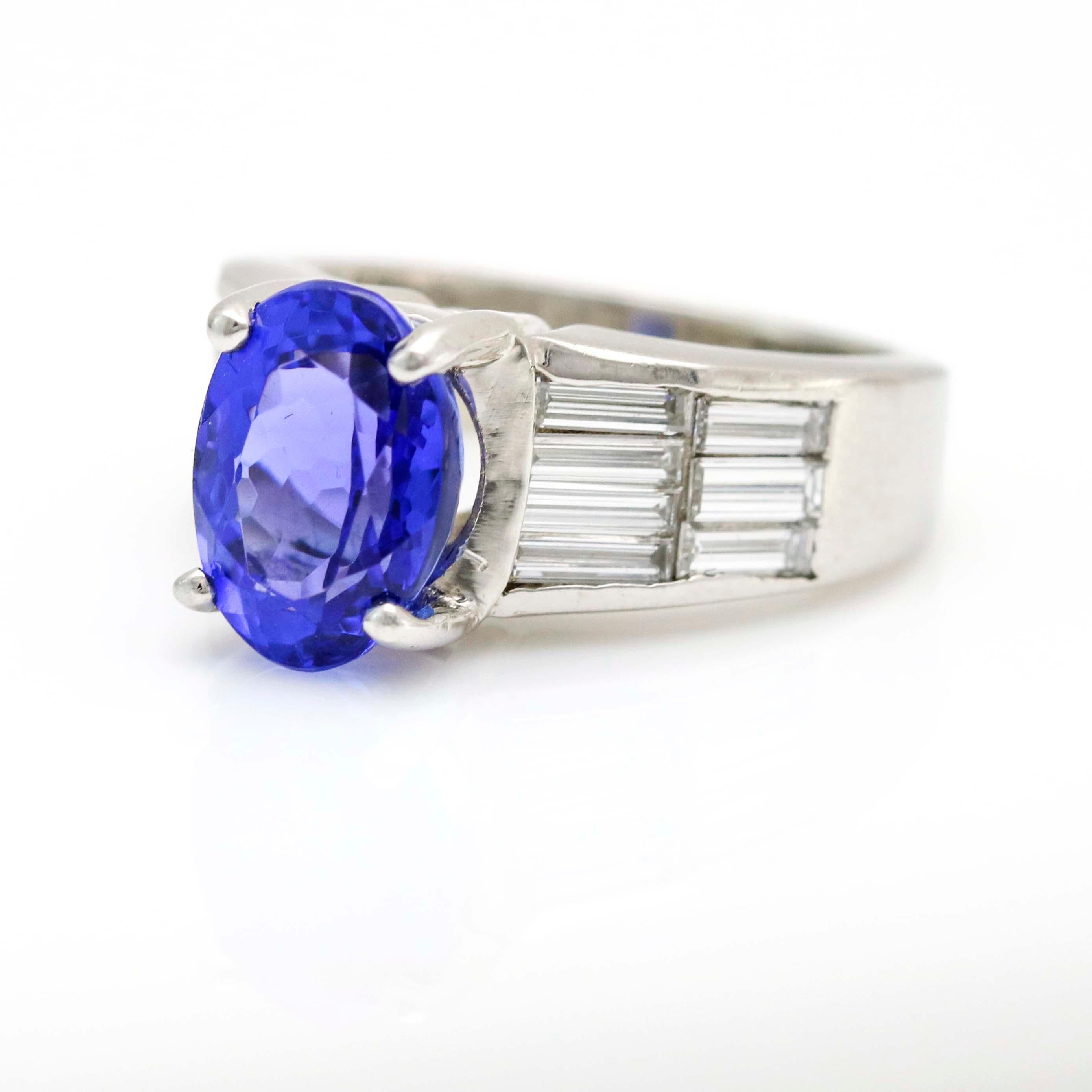 Retro oval Tanzanite cocktail ring with baguette cut diamonds side stone crafted of platinum. Estimated diamond total carat weight, 1 carat. Tanzanite, 10.5mm x 7mm x 6mm. Height from finger, 8mm. Size 5. Signed ADJ.