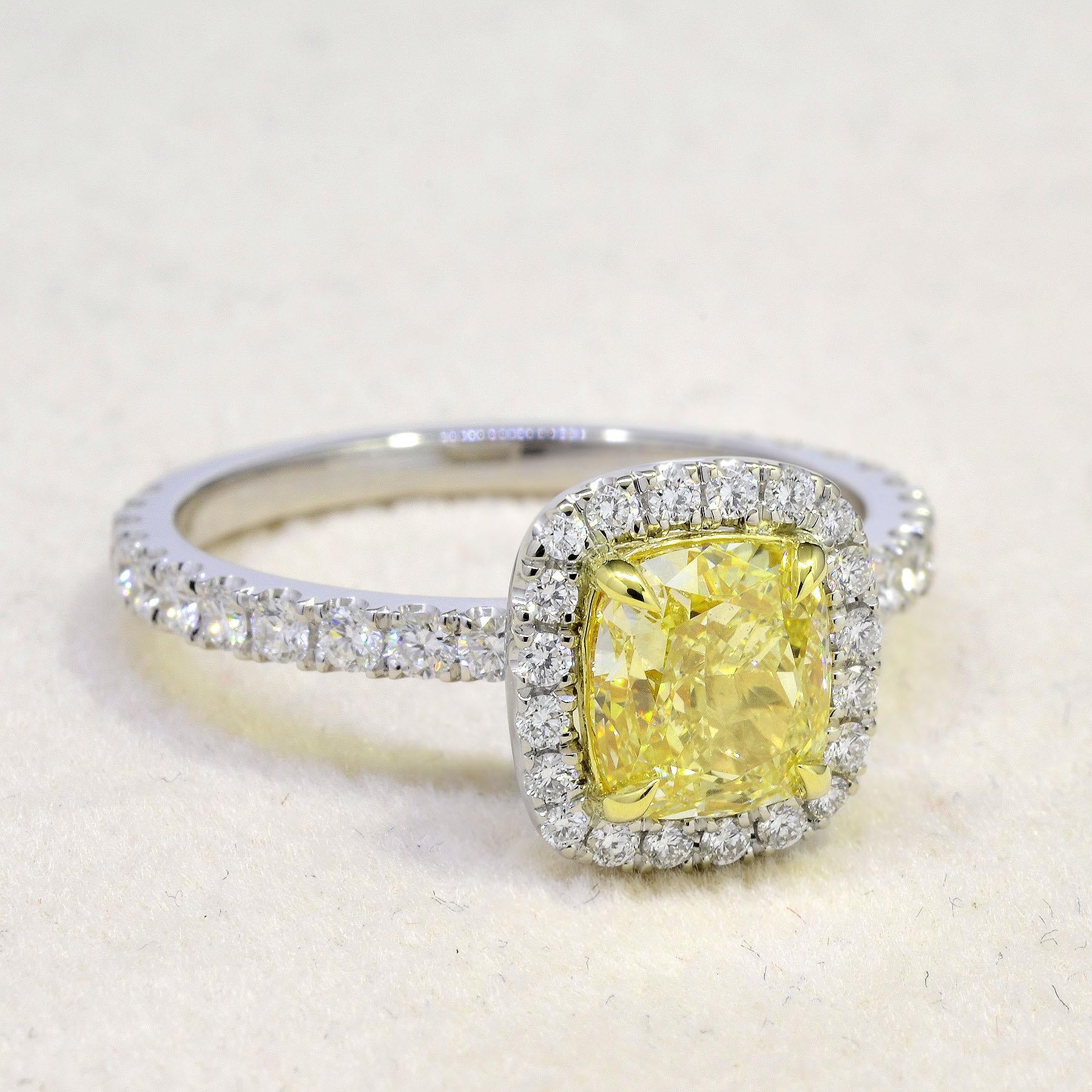 This fabulous Canary Fancy Yellow Halo Cushion Cut Engagement Ring has a 1.70 Ct. Cushion cut center diamond with Natural Fancy Yellow color and VS2 clarity. Surrounding the center stone and lining around the shank is 0.90 carat U-pave set Round cut