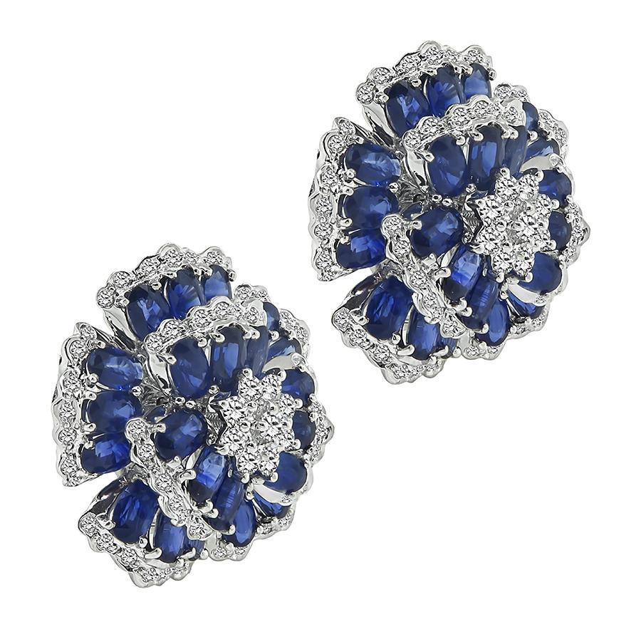 This is a stunning pair of 18k white gold flower earrings. The earrings feature lovely oval cut sapphires that weigh approximately 14.00ct. The sapphires are accentuated by sparkling round cut diamonds that weigh approximately 2.60ct. The color of