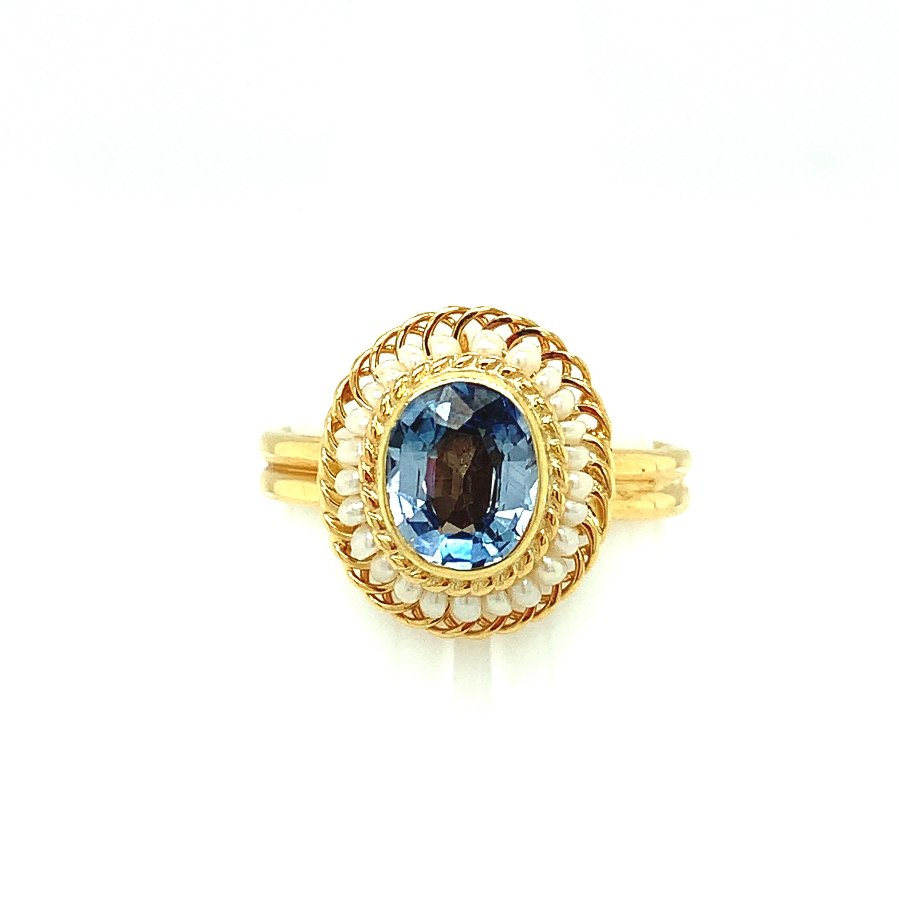 A bright and lively 2.61 carat oval blue sapphire is featured in this beautiful 18k yellow gold cocktail ring. This lovely ring was made by hand using the intricate art of filigree, using fine 18k yellow gold wire to thread and wrap seed pearls into