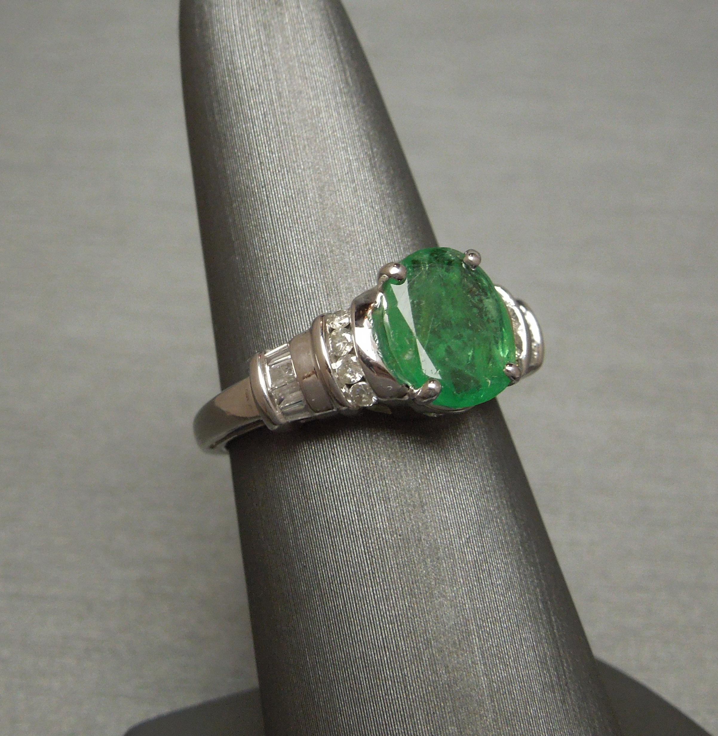 In an Engagement style solitaire, featuring a central 2.63 carat Oval Light-Medium Green Emerald secured in 4 prongs accented with a total of 0.57 carats of Channel set Brilliant and Baguette cut Diamonds ranging from a Nearly Colorless F-G Color &