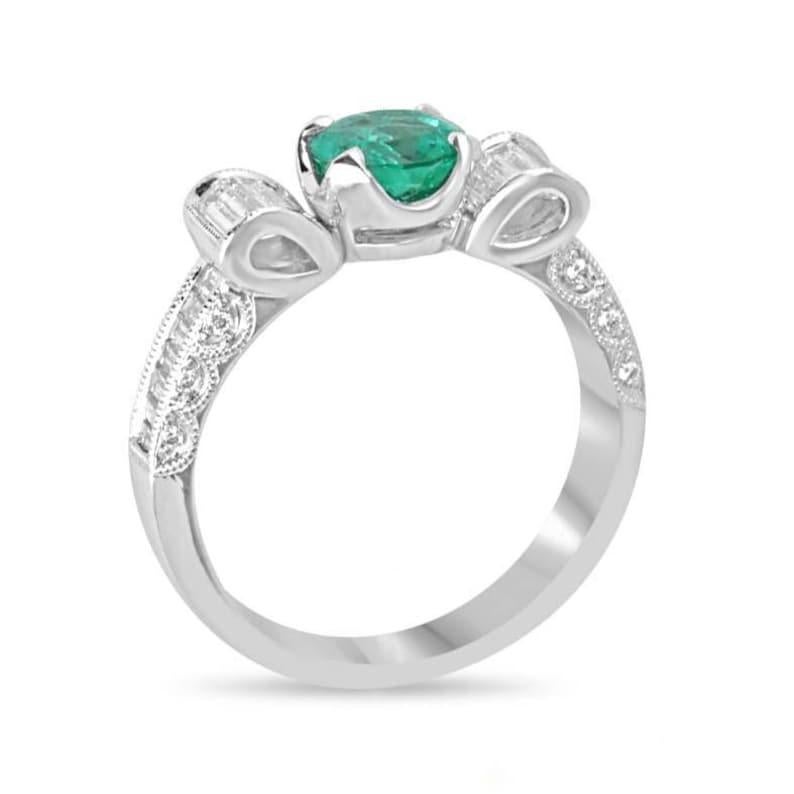 This exquisite engagement ring showcases a stunning round-cut emerald, renowned for its vivid green color, transparent clarity, and exceptional luster, securely set in a classic four-prong setting. Surrounding the emerald, a captivating bow design
