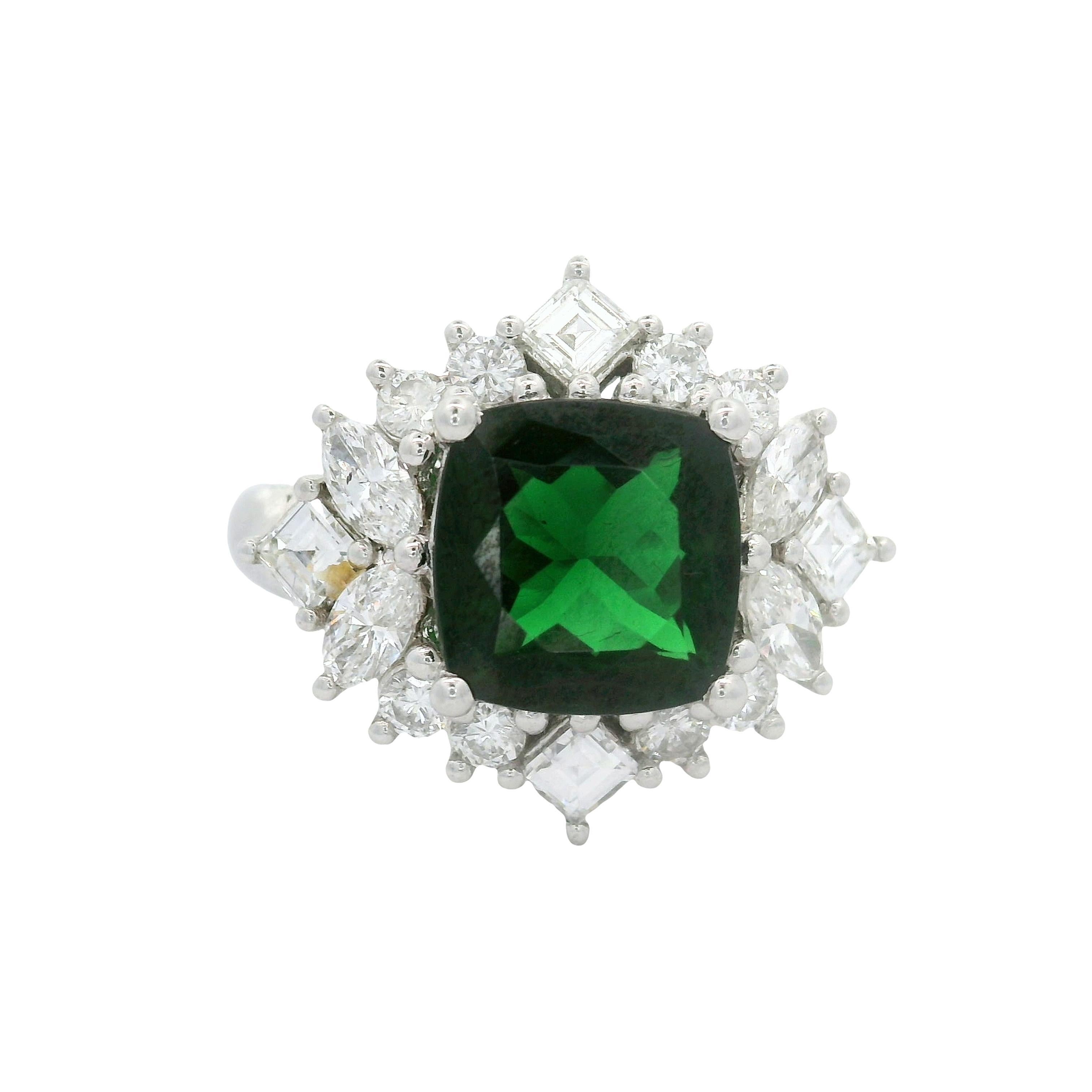 Un anello sorprendente con un'affascinante tsavorite da 2,64 carati con taglio a cuscino, che emana una profonda tonalità verde. Questo vibrante centro è elegantemente circondato da 1,05 carati di diamanti a taglio misto, ciascuno con un colore