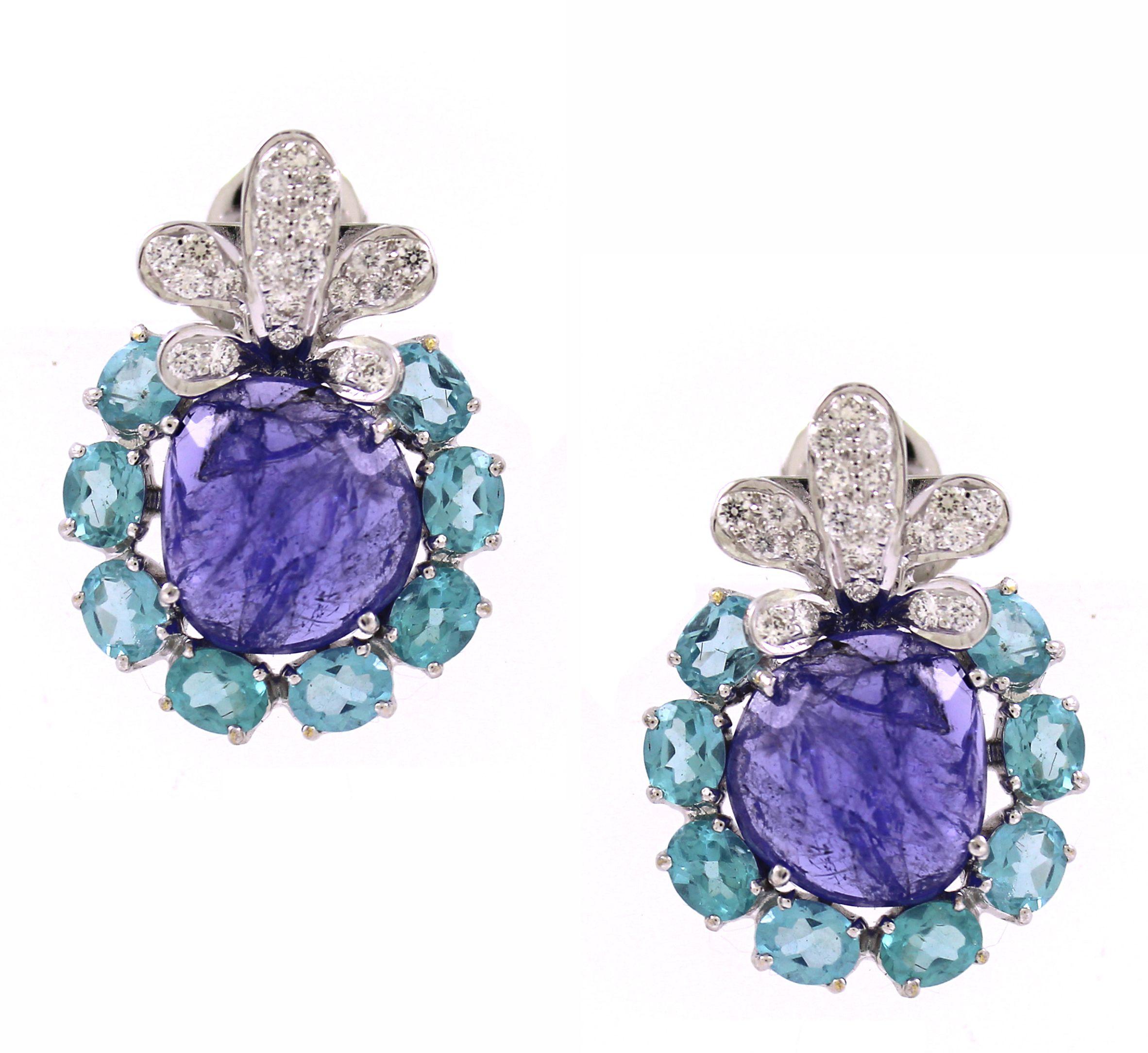 Questo squisito set di ciondoli, composto da un paio di orecchini e da un ciondolo abbinato, irradia opulenza e intricata maestria. Il cuore è costituito da tre splendide tanzaniti ovali blu-violacee, per un totale di 26,56 carati, che emanano