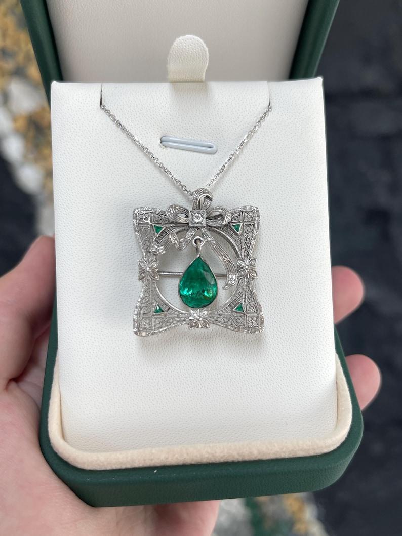 This exquisite multifunctional brooch and pendant is a true vintage treasure, likely dating back to the early to mid-1900s, showcasing an elegant, timeless design. At its center, a bezel-set, pear-cut Colombian emerald with a rich green hue dangles