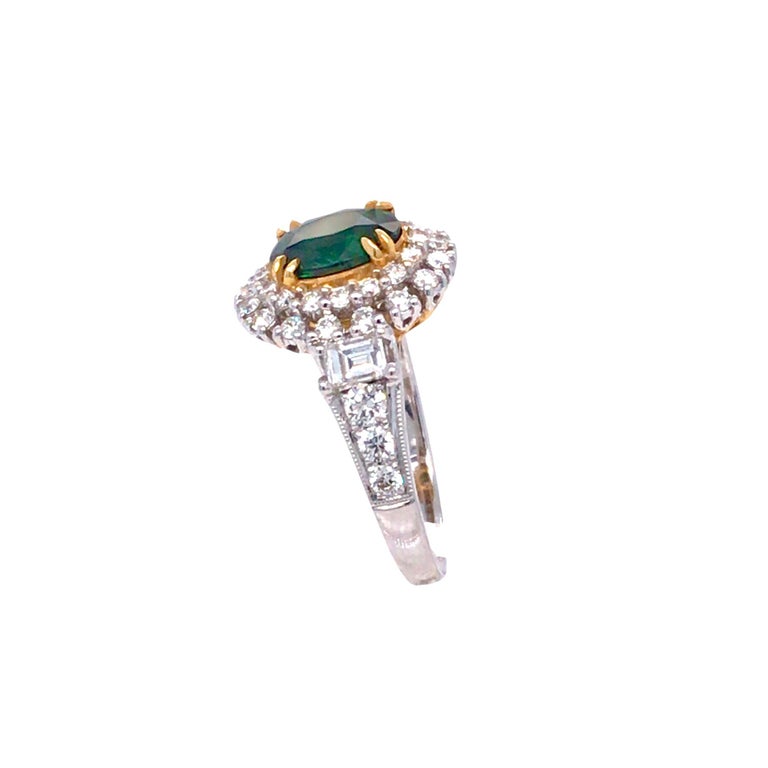 This gorgeous ring has an oval cut green tsavorite garnet center, set in 18k yellow gold, surrounded by a double halo of round diamonds, with the main body of the ring set in 18k white gold. Two diamond baguettes decorate the shoulders of the