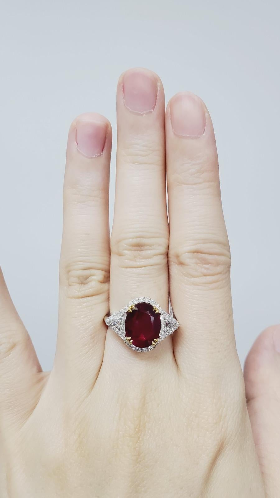Set with an oval-shaped ruby, weighing 2.66 carats, flanked on either side by two triangular-shaped diamonds totaling 0.64 carats, surrounded by round brilliants totaling 0.31  carats and mounted in 18k white gold, ring size 6½.

Accompanied by