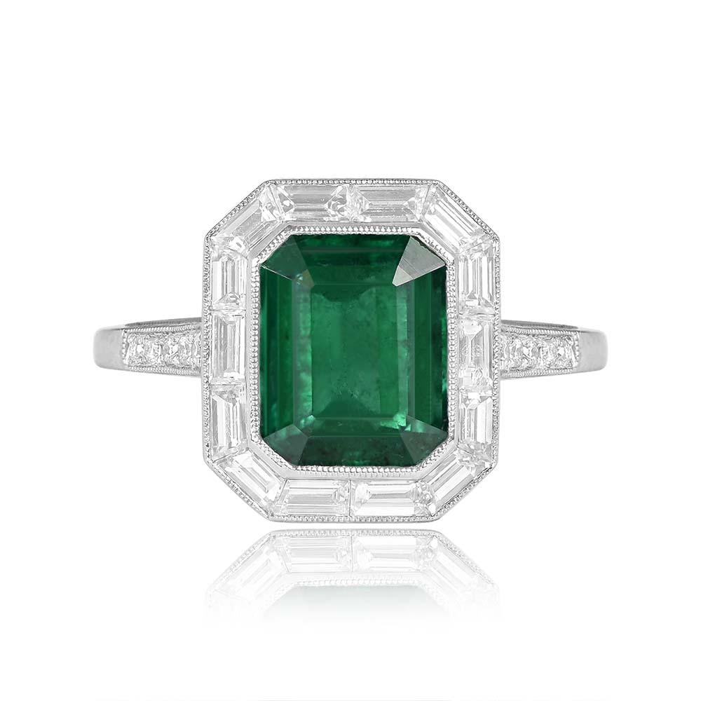 This elegant ring showcases a mesmerizing 2.66-carat emerald-cut emerald at its center, bezel-set to highlight its rich, vibrant hue. Encircling the centerpiece is a refined halo of baguette-cut diamonds, meticulously set and weighing approximately
