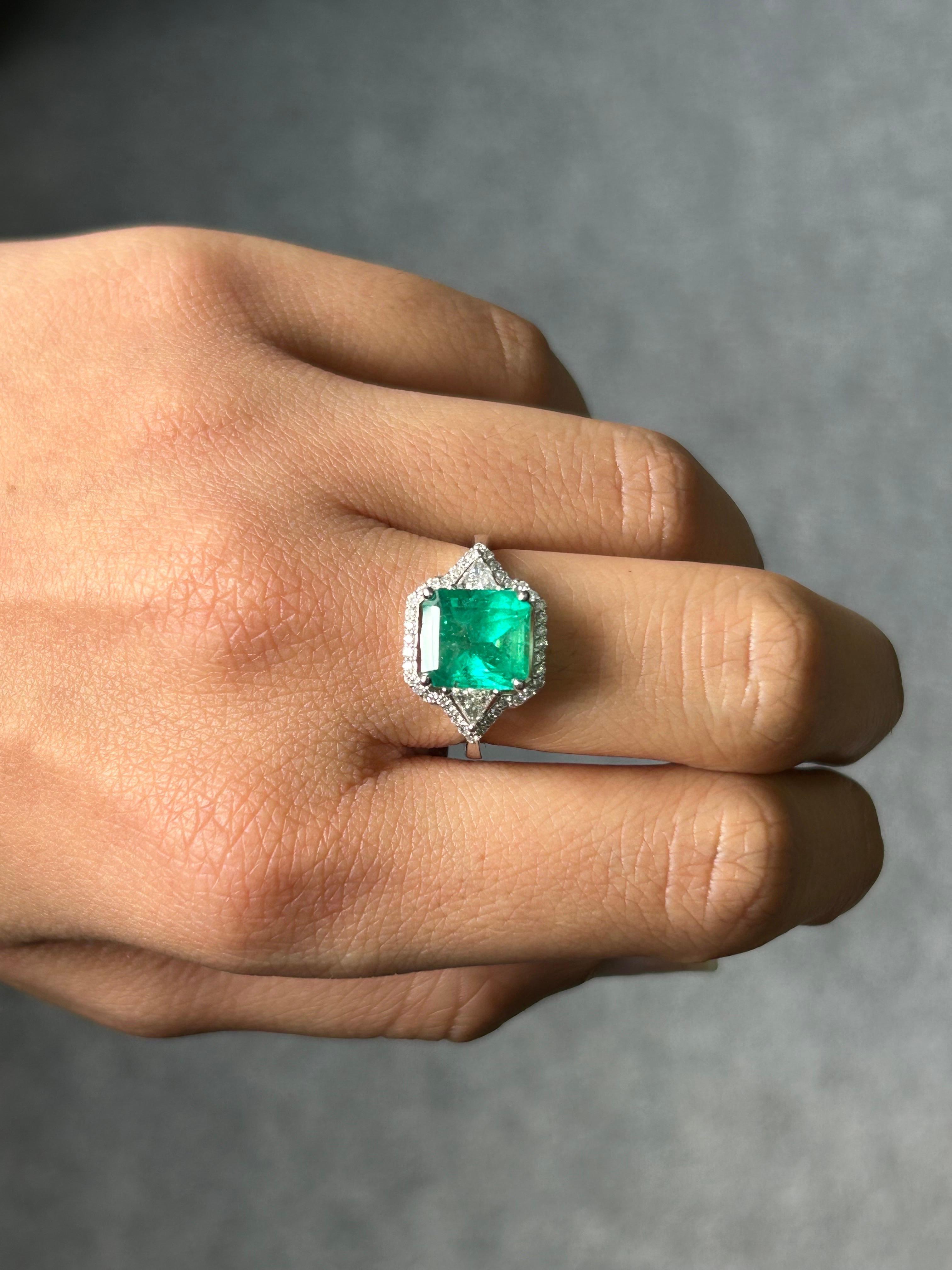 A certified vibrant, vivid green 2.36 carat emerald cut Colombian Emerald and 0.2 carat VS quality Trillion Diamond and 0.22 carat round Diamond halo three stone, engagement ring. The stones are set in 18K White Gold. Currently sized at US 7, can be