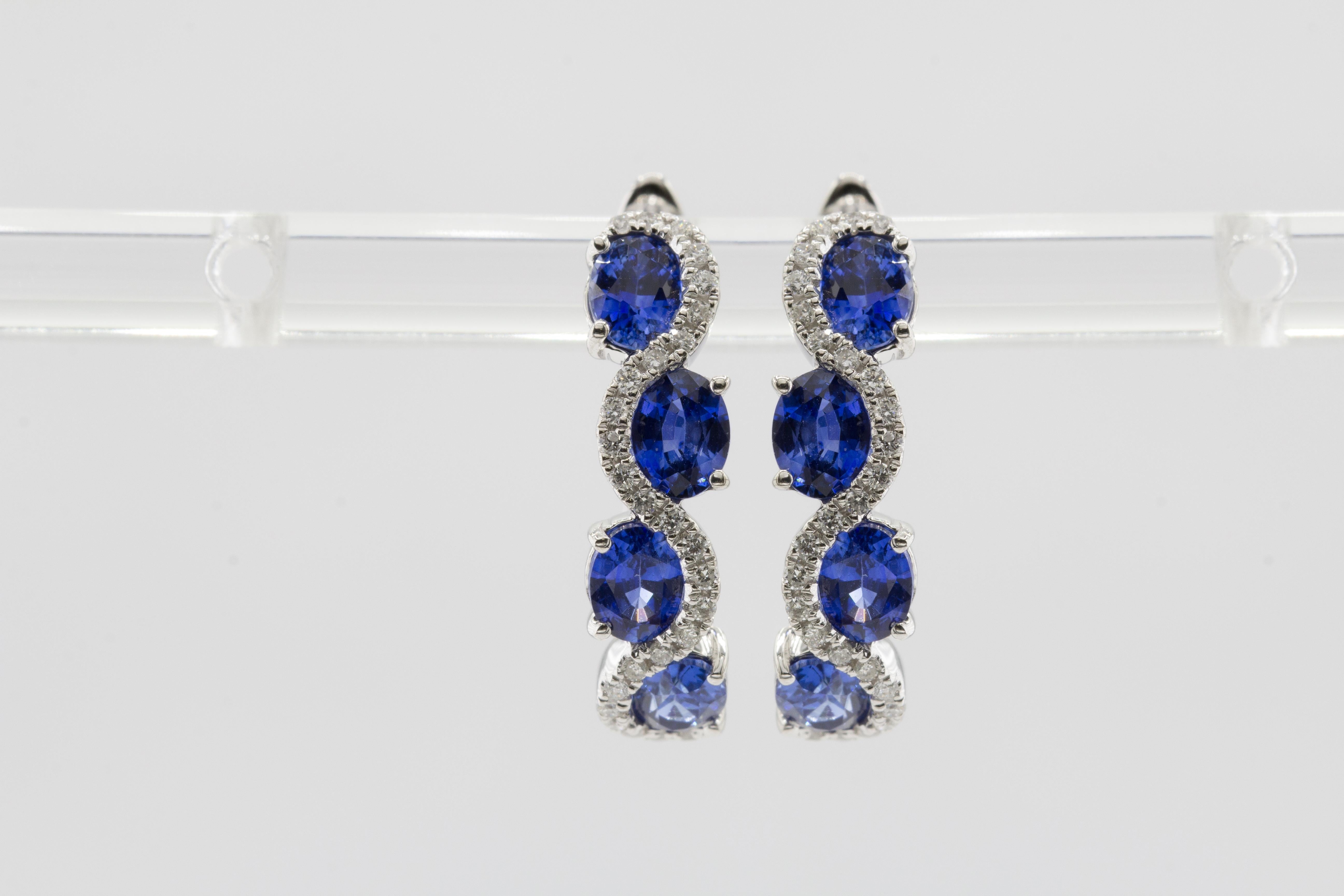 At DiamondTown, we proudly present these exquisite earrings, where each one showcases a harmonious dance of four oval-cut vivid blue sapphires, boasting a combined weight of 2.69 carats. These captivating sapphires are elegantly embraced by a