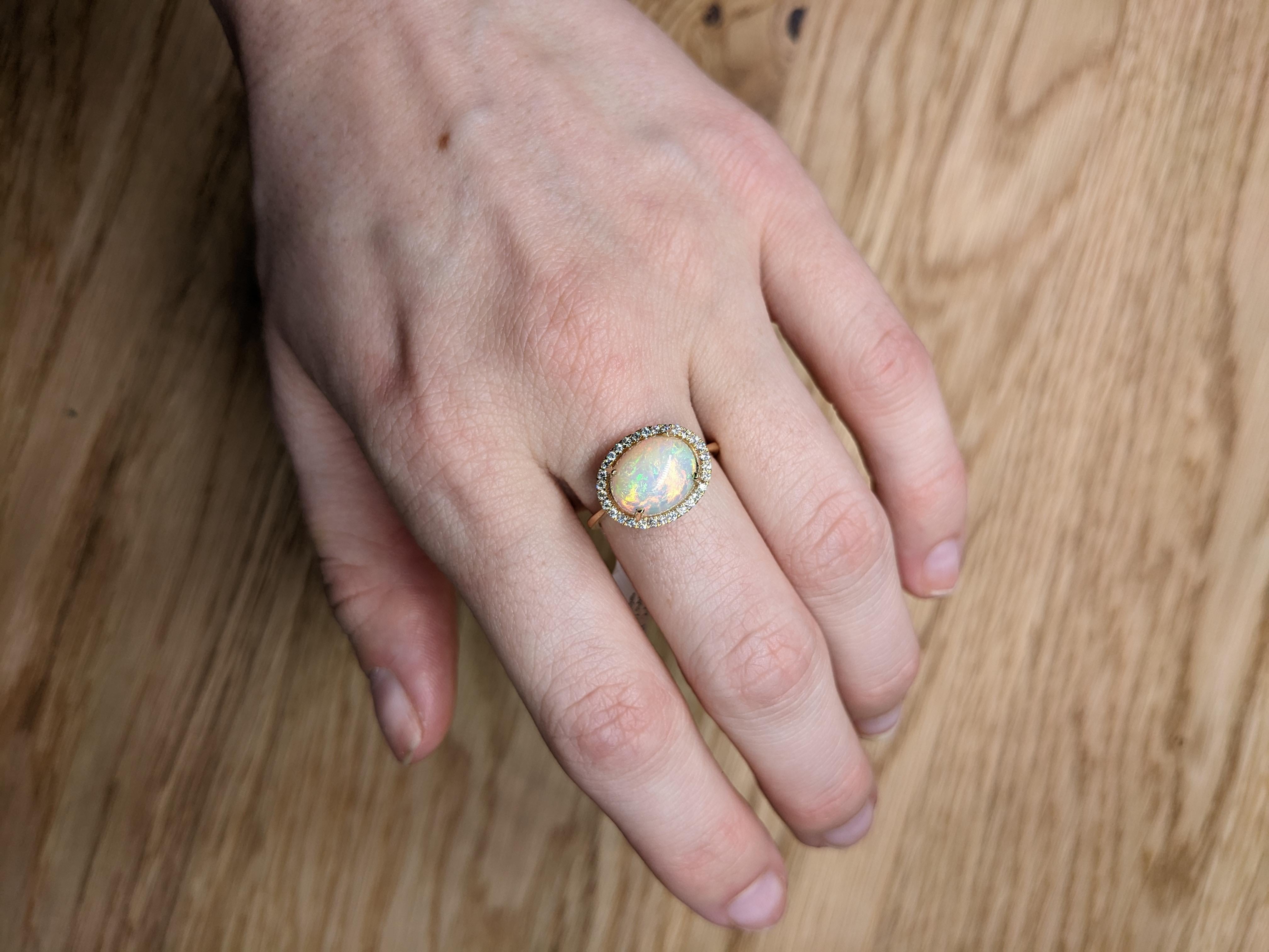 La bague est un chef-d'œuvre époustouflant, mettant en vedette une captivante opale de 2,64 carats dans une élégante forme ovale (12x9 mm). Sertie dans un luxueux or jaune 14K, cette opale est entourée d'un halo de diamants éblouissants qui