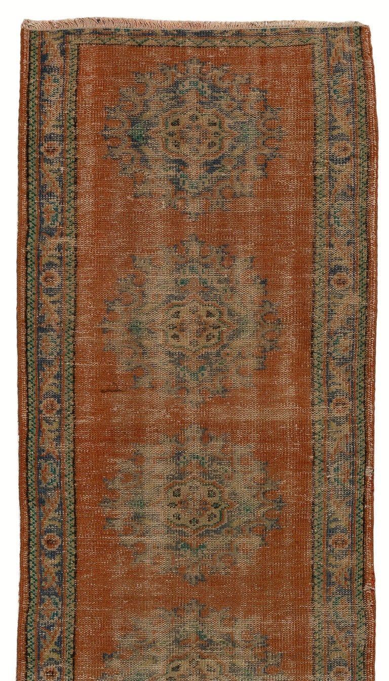 Vintage Turkish runner rug with a design of multiple medallions in slate blue and emerald green against a plain field in rust red as well as a slate blue border. It was hand-knotted in Turkey in 1960s with low wool pile on cotton foundation. In good