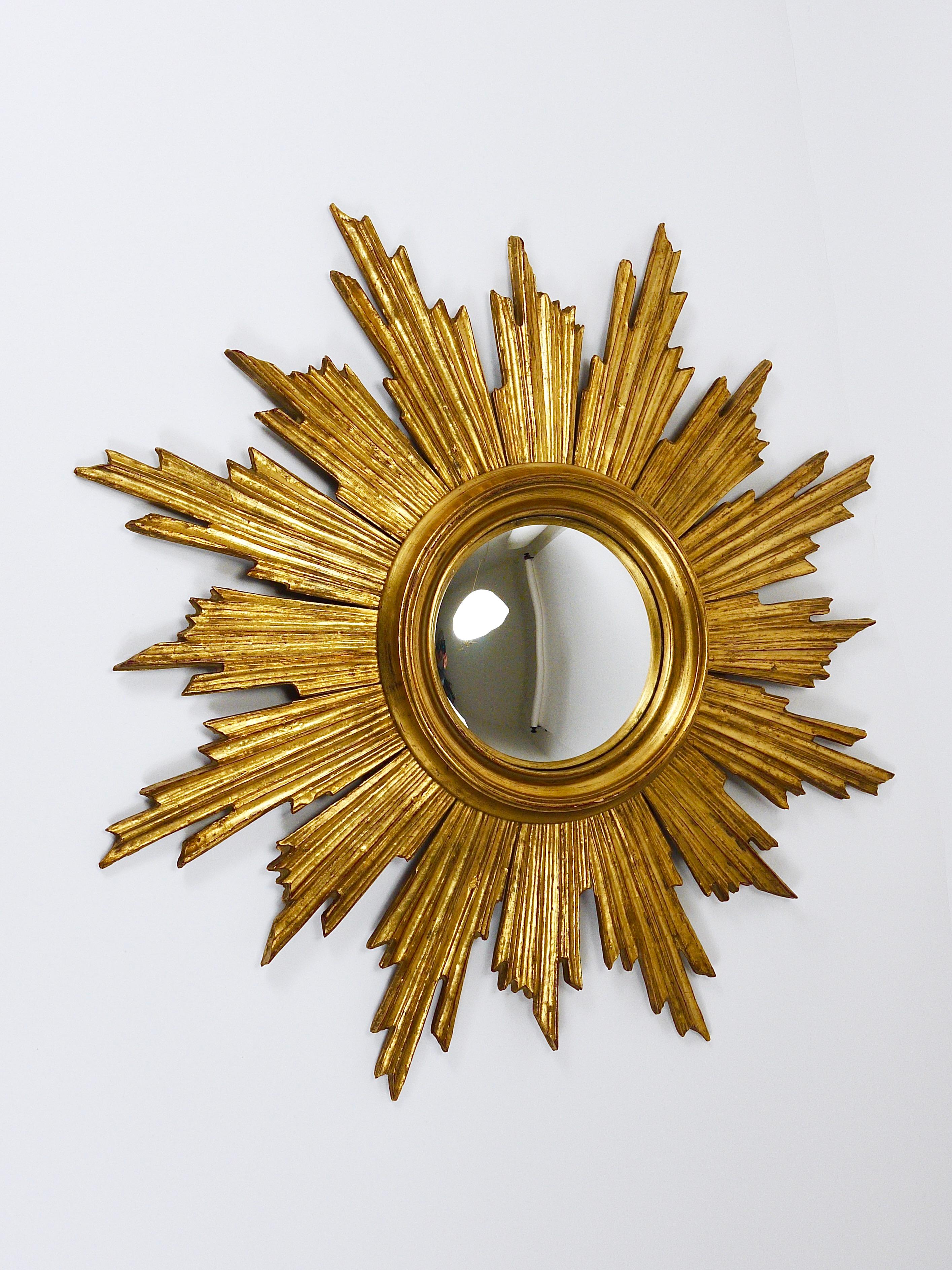 Elegante y gran espejo decorativo francés soleil de mediados de siglo, fabricado en Francia en la década de 1950. Esta exquisita pieza presenta un marco de madera tallada a mano adornado con rayos dorados alrededor del espejo. El espejo tiene un
