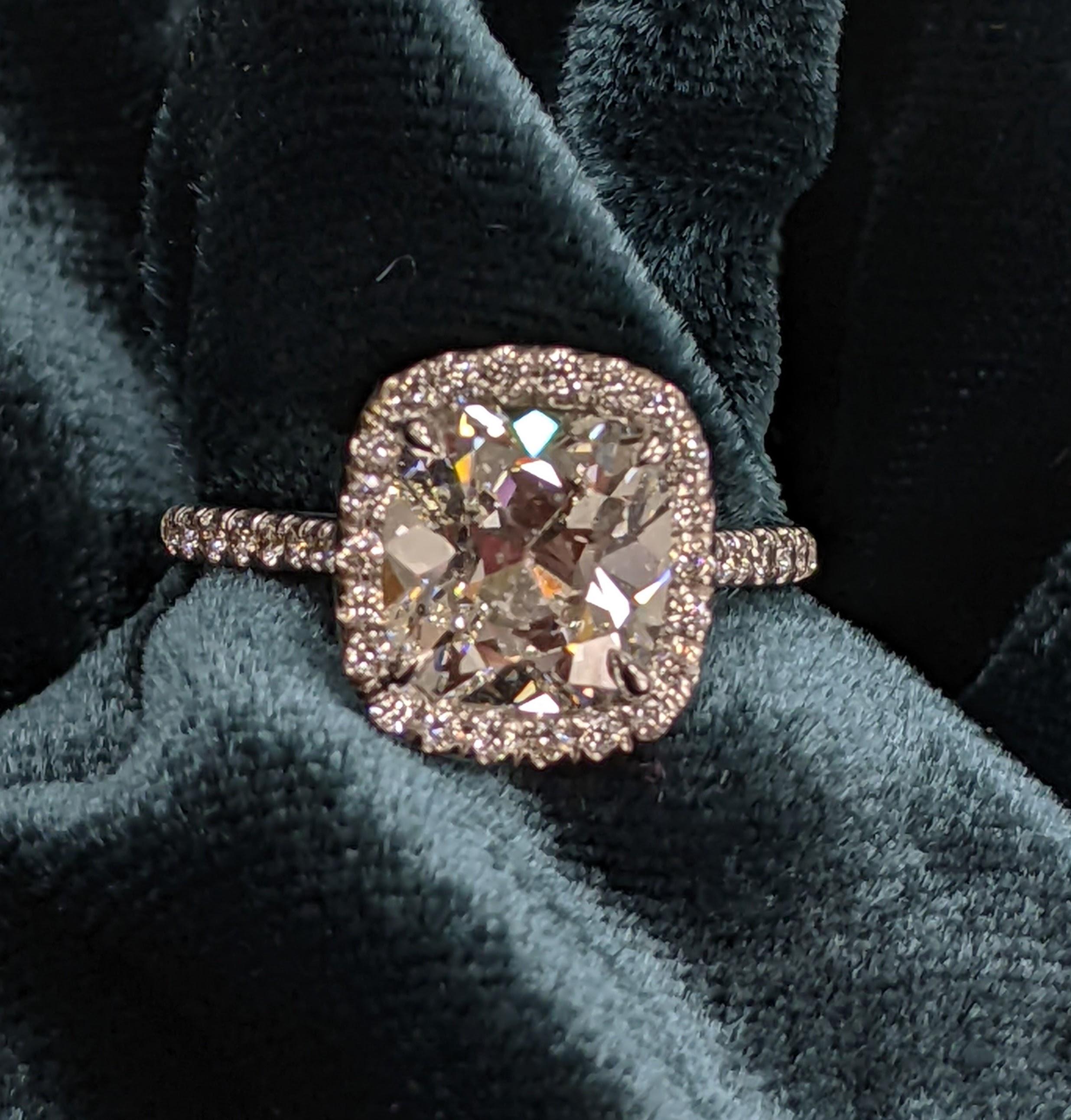 2.73 Cushion Cut graded with a G color and SI-2 clarity (and eye clean to boot) from GIA.  This old miner-styled stone is surrounded by a halo of small diamonds which extends into the ring's 18KT White Gold mounting, totaling up to 38 small diamonds