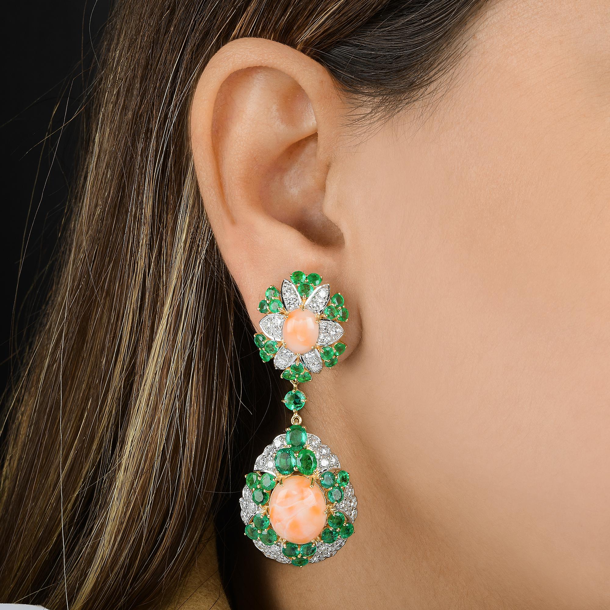 Estos Pendientes Colgantes de Oro Amarillo de 14 Kilates con Coral Esmeralda Diamante de 27,08 TCW tienen una gema de coral de talla ovalada tachonada en el centro con esmeralda y diamantes engastados a lo largo, formando un óvalo floral en la parte