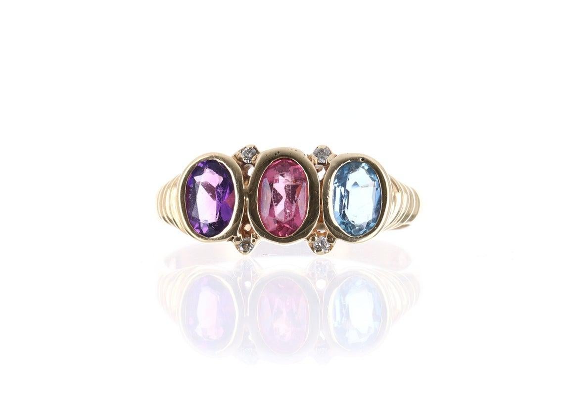 Showcased is a superb natural three birthstone ring that is full of life and exuberance from any view. A beautiful amethyst, pink topaz, and an aquamarine are the center of attention as they are bezel set and sit closely. The soft tones are warm and