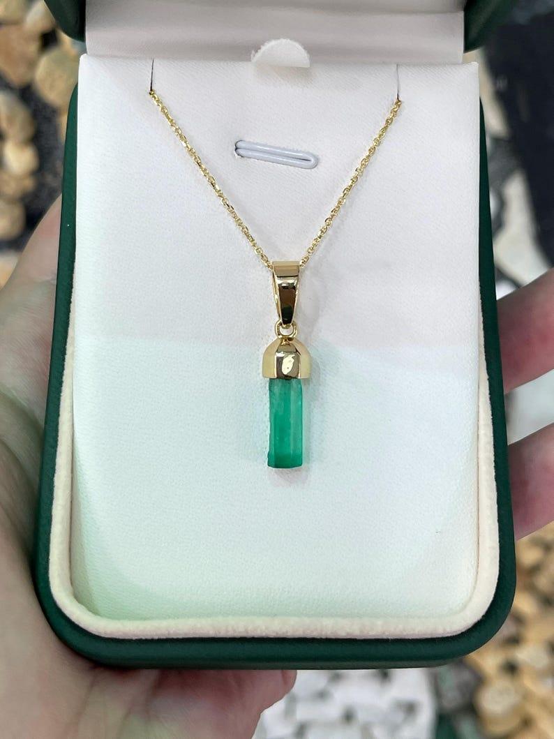 Ti presentiamo il nostro ciondolo con smeraldo grezzo naturale, un pezzo distintivo e unisex che mostra la bellezza grezza di un cristallo di smeraldo terminato da 2.71 carati proveniente dai paesaggi verdeggianti della Colombia. Il cristallo grezzo