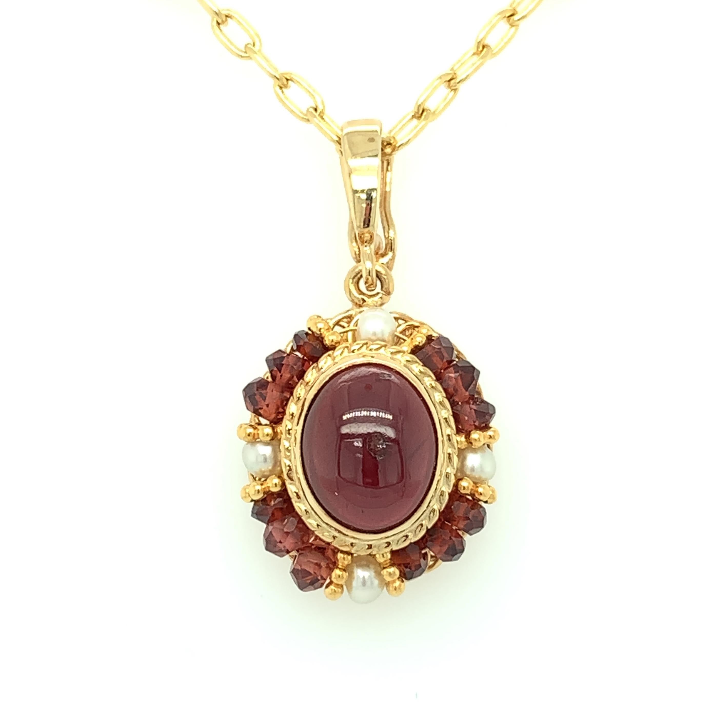 This pendant features a beautiful oval garnet cabochon in an intricate design of handmade 18k yellow gold filigree. The richly colored garnet is bezel set and framed by a halo of seed pearls and delicate garnet beads that have been hand strung on