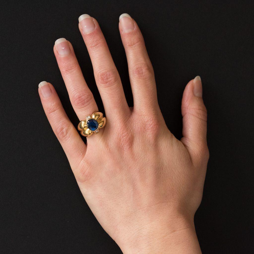 Ring in 18 karat yellow gold, eagle head hallmark. 
This multi lobed shape ring is composed of half-moon shapes featuring an oval sapphire with a bezel set princess cut diamond on each side.
Sapphire weight: approximately 2.75 carat 
Total diamond