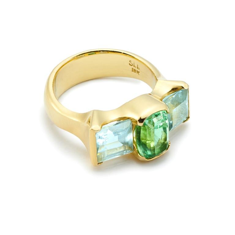 A contemporary twist on a more traditional three stone ring. The sultry 2.75 Carat Mint Tourmaline, said to attract inspiration and compassion, is nestled between 3 Carats of square cut Aquamarine, thought to promote calm. Set in 18 Karat Gold, the