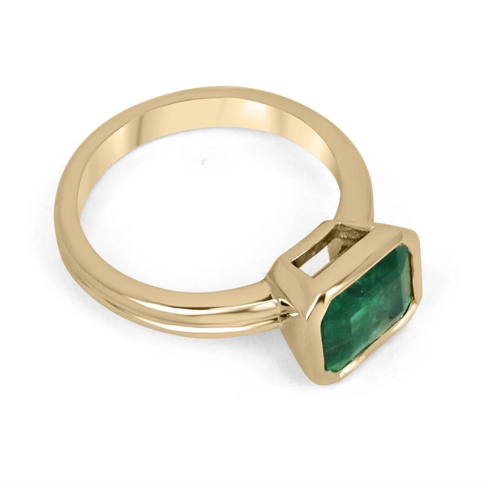 Displayed is a stunning East-to-West emerald solitaire engagement or right-hand ring in 14K yellow gold. This gorgeous solitaire ring carries a 2.75-carat emerald in a bezel setting. Fully faceted, this gemstone showcases excellent shine and