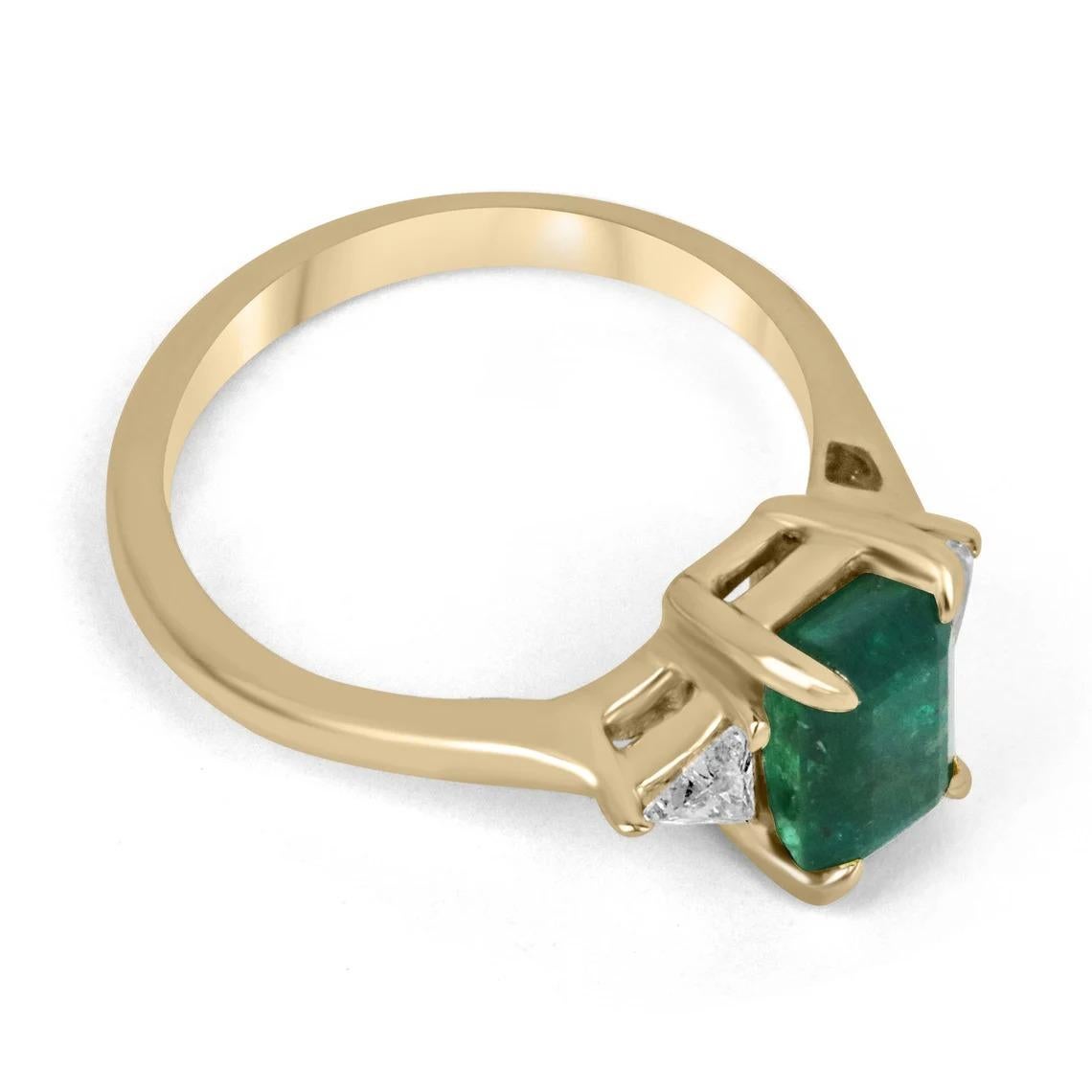 A luxurious emerald and diamond three-stone ring. This magnificent piece features a remarkable emerald cut emerald from the origin of Zambia as the center stone. The gem displays a dark, desirable emerald green color with very good transparency and